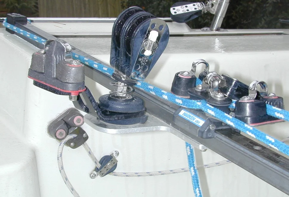 Mainsheet Barney Post Equivalent (Mounted on Traveller instead of Cockpit Floor) - Side View Aluminum bracket bolted to Harken hi-beam traveler supports swivel mount for double ratchet main sheet block and double cam cleat for dual ratio mainsheet system from Layline. Double-ended backstay line and cleat on cockpit side beyond.
