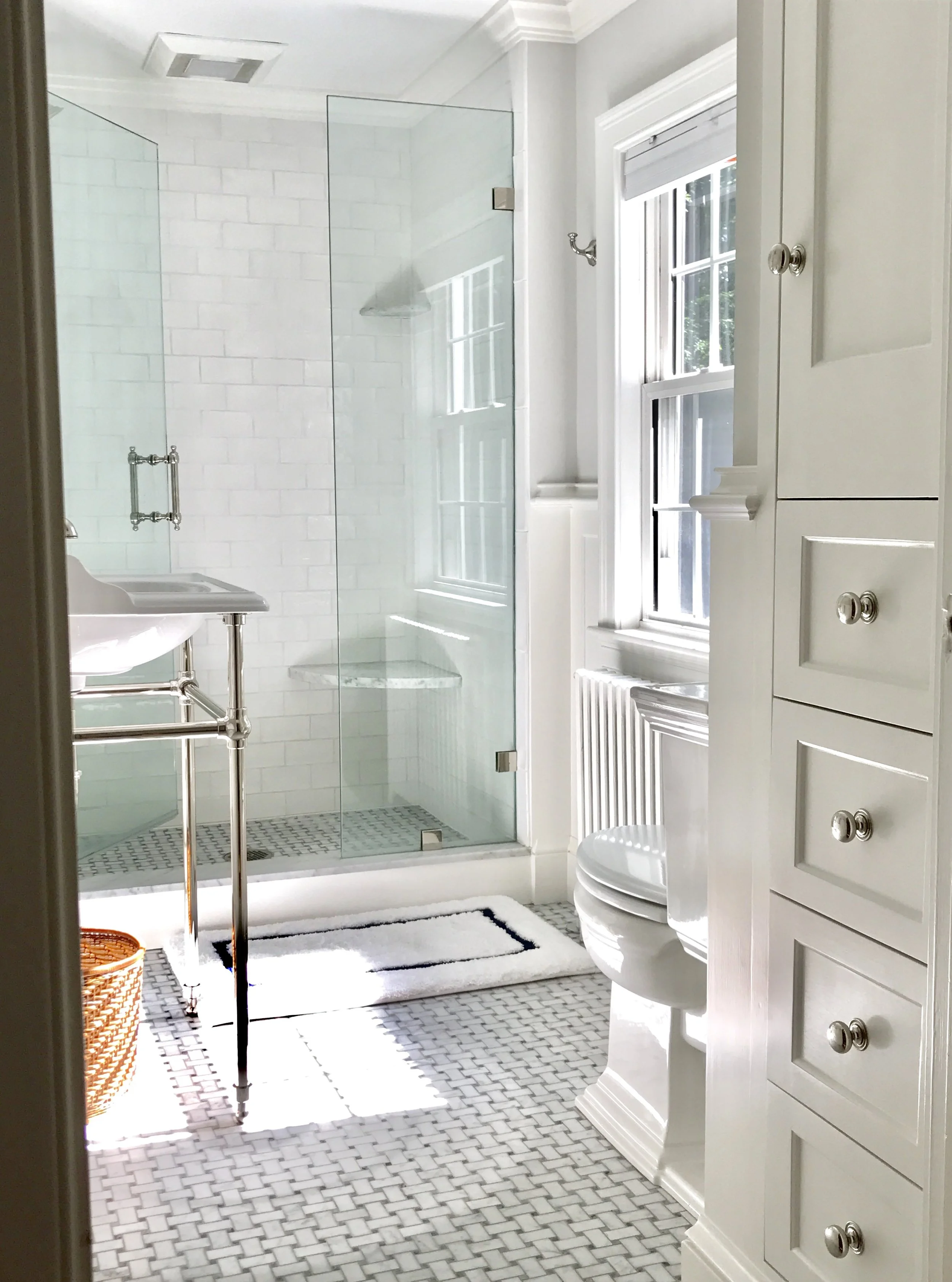 Newly renovated bathroom. A custom shower replaced the old circa 1941 bath tub. Carrara marble seat adds comfort with the ease of cleaning. Traditional marble basket weave floor tiles added a timeless look along with the new console sink and polished nickel fixtures by Perrin & Rowe.