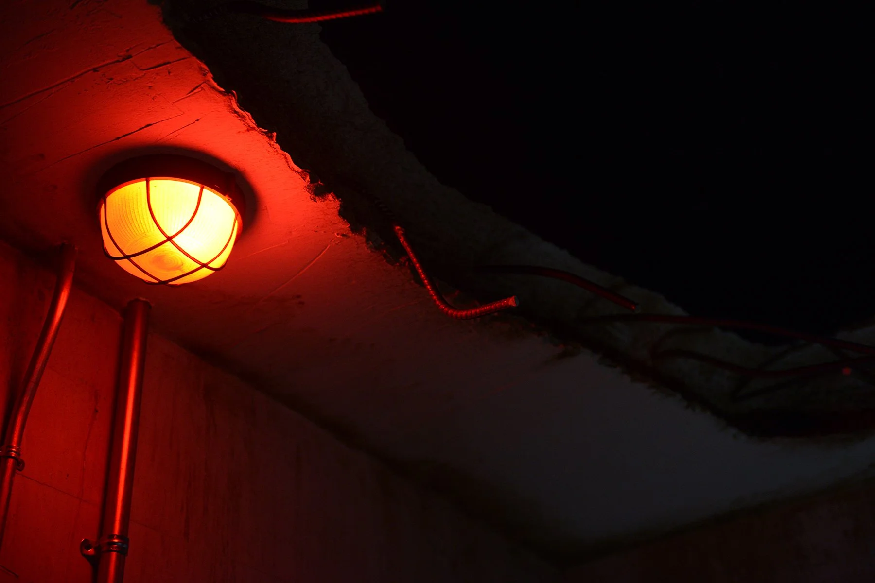 A red light illuminates the remains of a collapsed concrete ceiling with rebar jutting from the jagged rubble