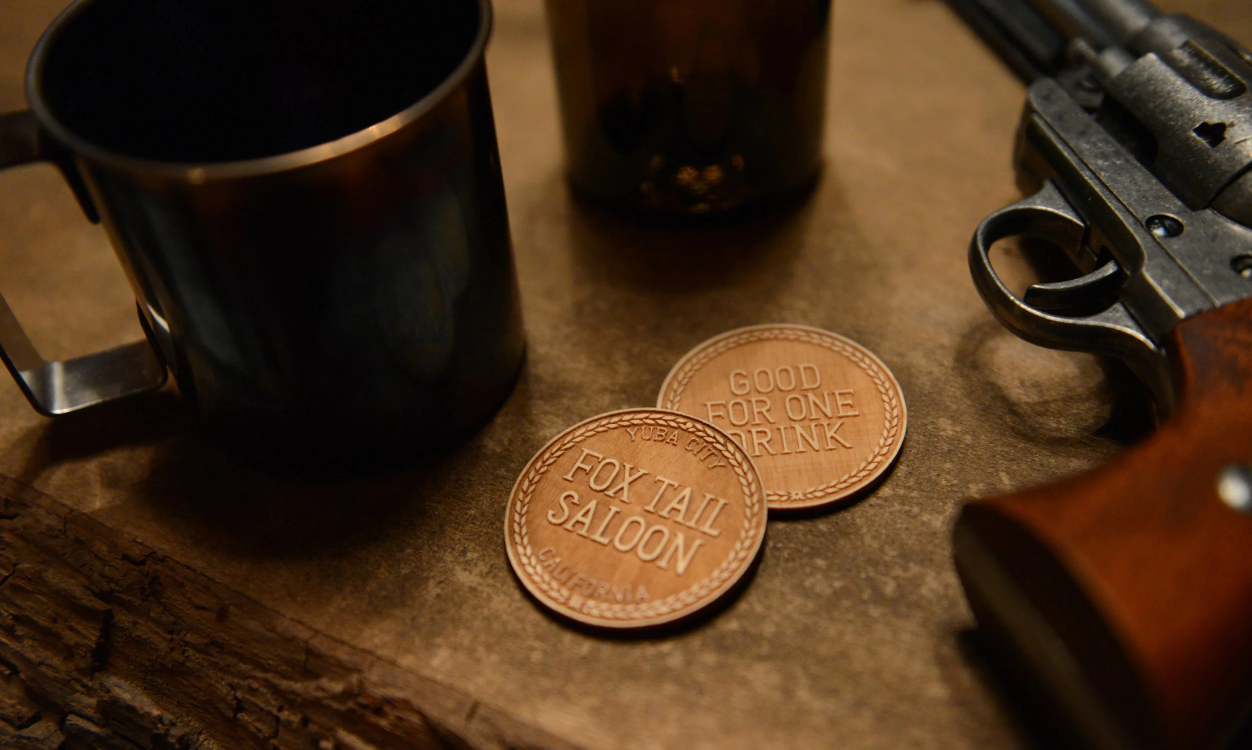 A revolver, tin cup, beer bottle and drink tokens lay on the bar of the Fox Tail Saloon