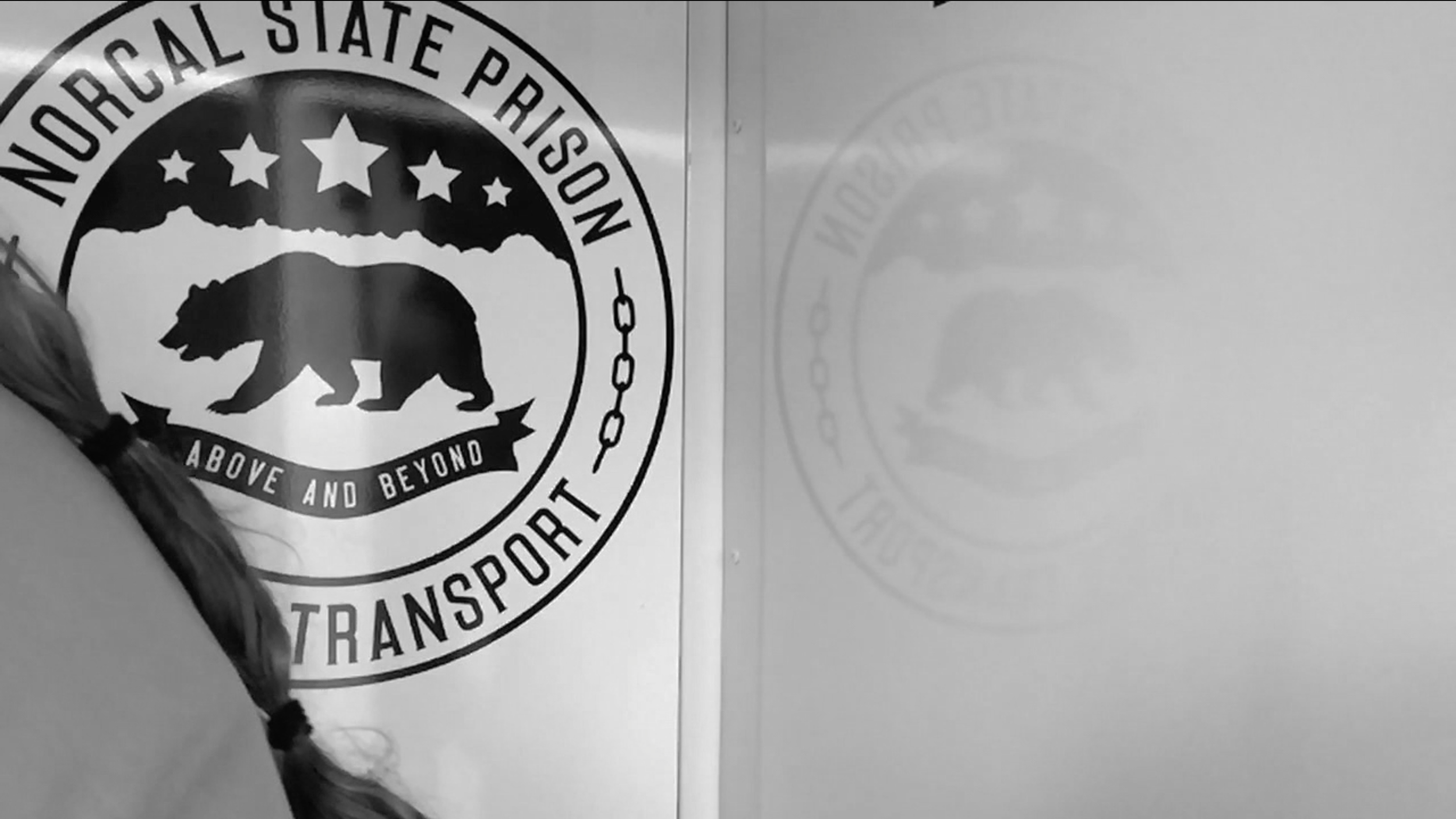 A convict sits in front of a seal that reads "NorCal State Prison Inmate Transport"