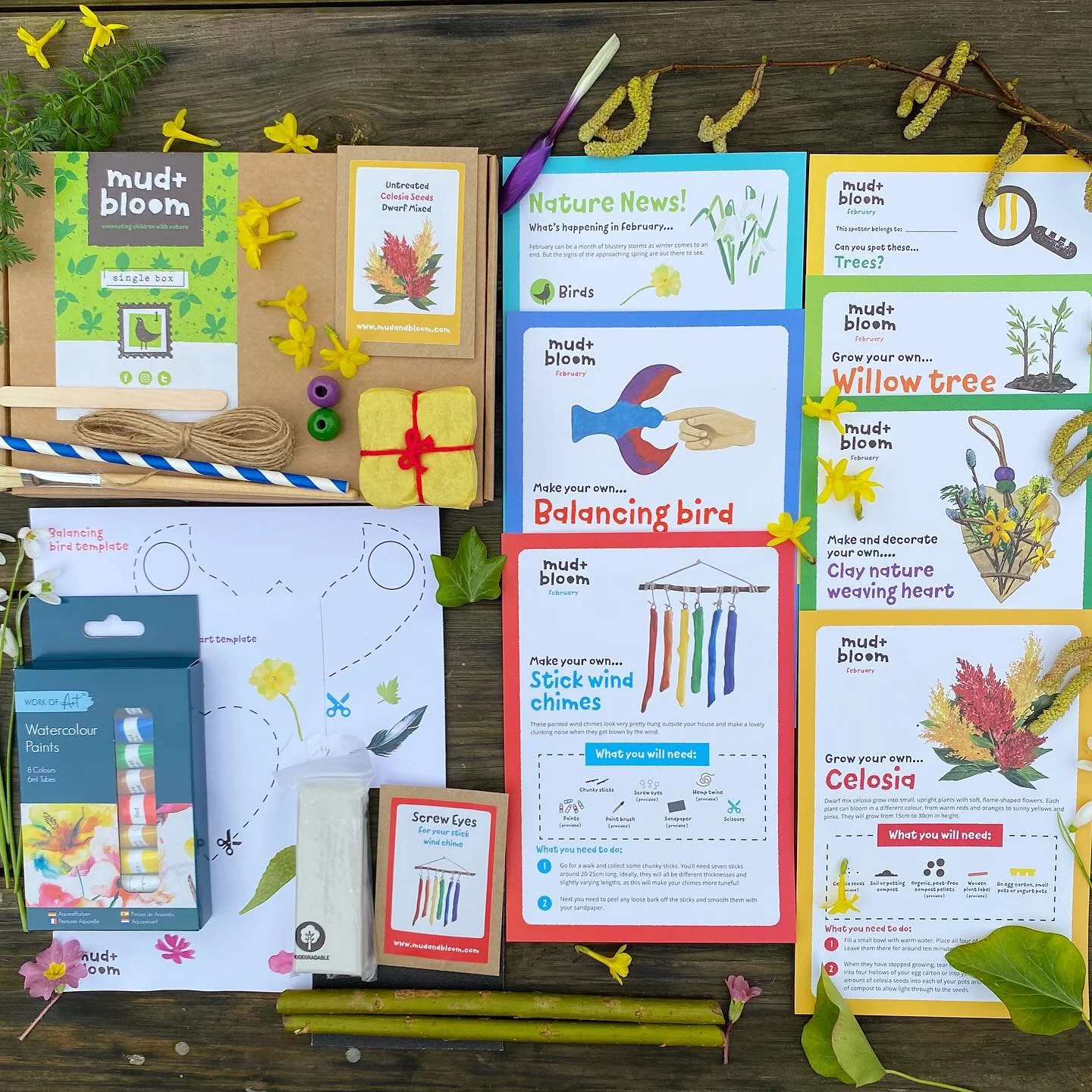 A collection of educational gardening and crafting materials for children, including plant seeds, craft supplies, instructional sheets for making a balancing bird, stick wind chimes, and a clay heart, all surrounded by small flowers and plants on a wooden surface.
