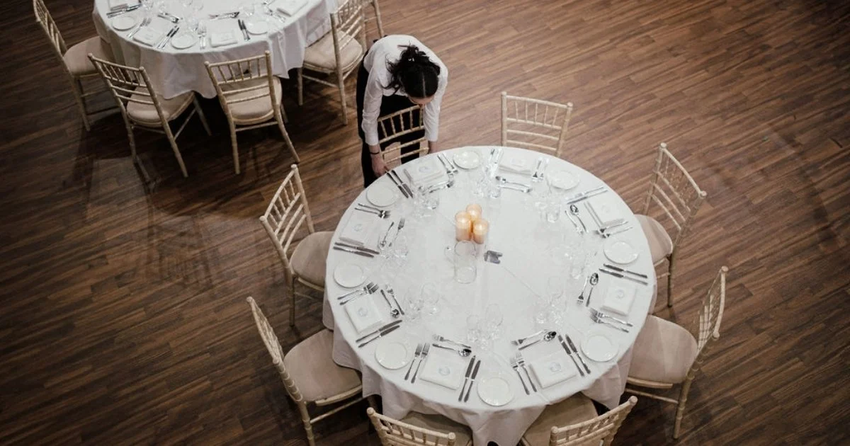 Front of house team member carefully straightening chairs before wedding guests arrive, preparing a wedding reception catered by Salters Events