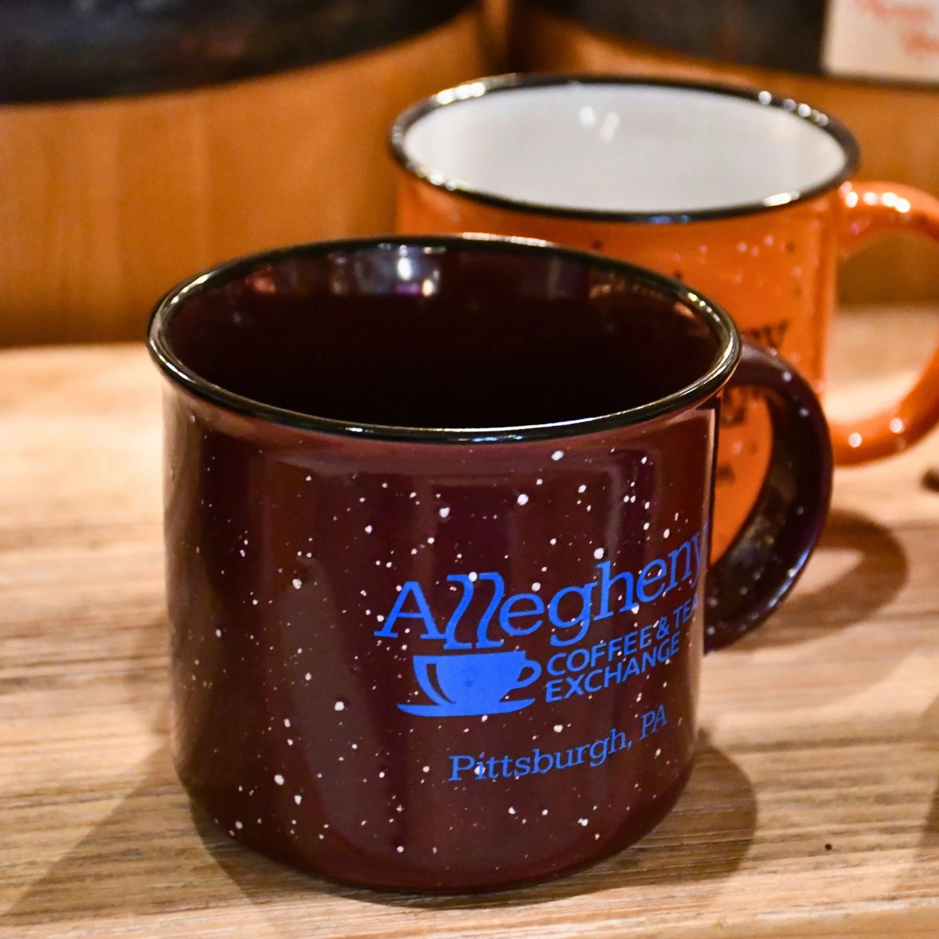  Allegheny Coffee &amp; Tea Exchange mugs sitting on wooden table at the coffee shop in Pittsburgh’s Strip District 