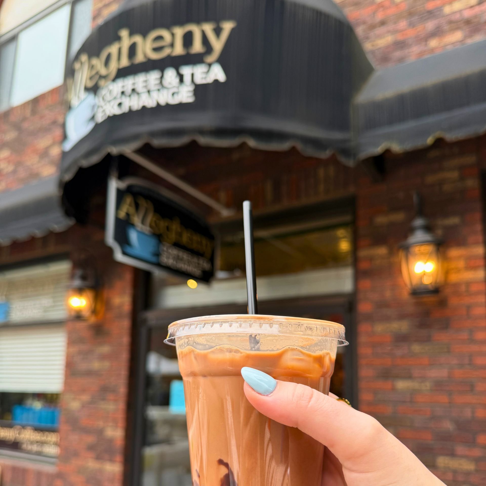  holding an iced coffee outside of the Allegheny Coffee &amp; Tea Exchange storefront 