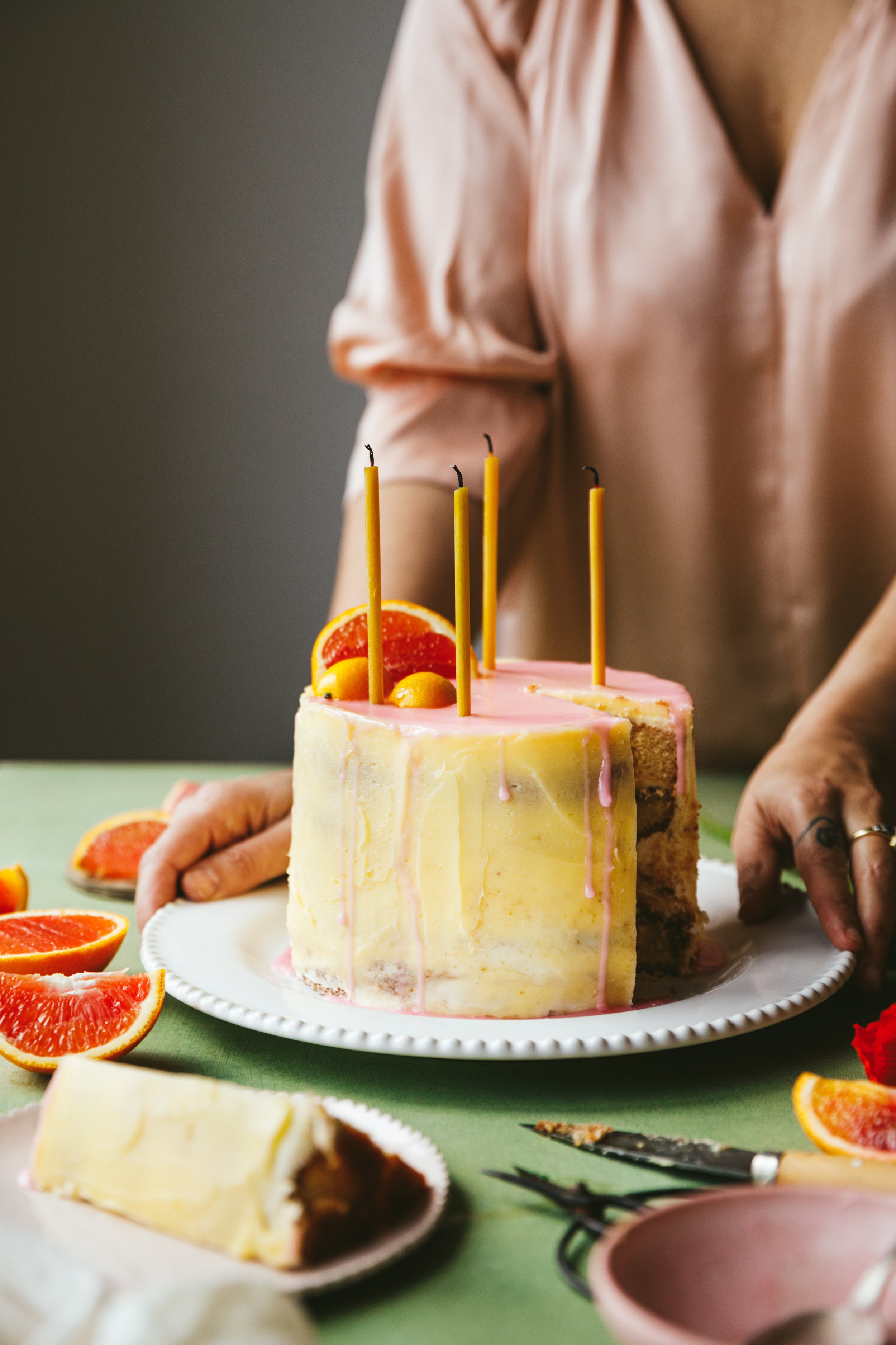 London videography workshop blog post image showing a person in the background holding a dish on a table with a layered cake with pretty yellow and pink icing, long candles and a garnish of orange slices and kumquat