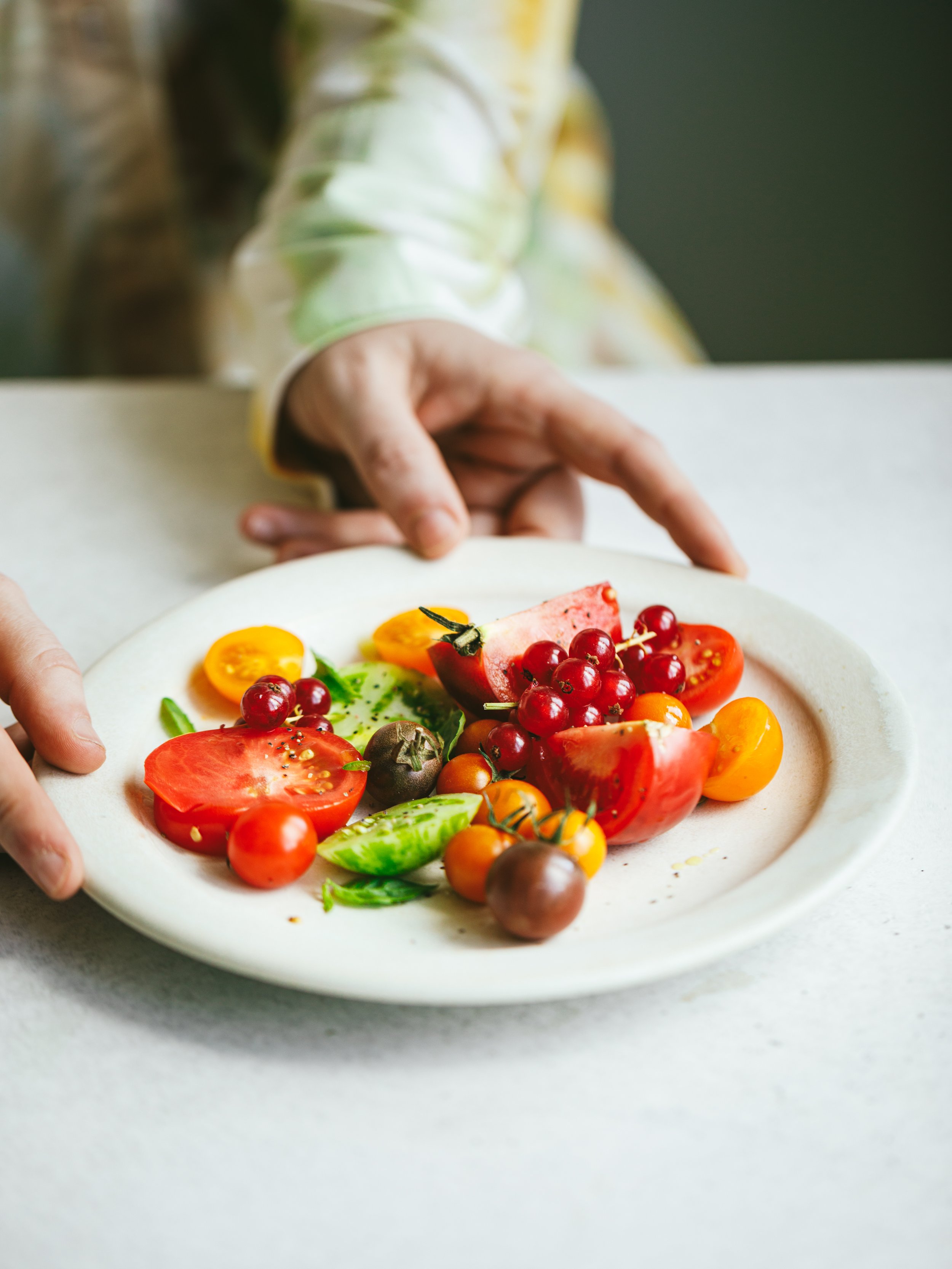 Blog post image showing hands holding a plate of pretty, colourful sliced tomatoes and berries