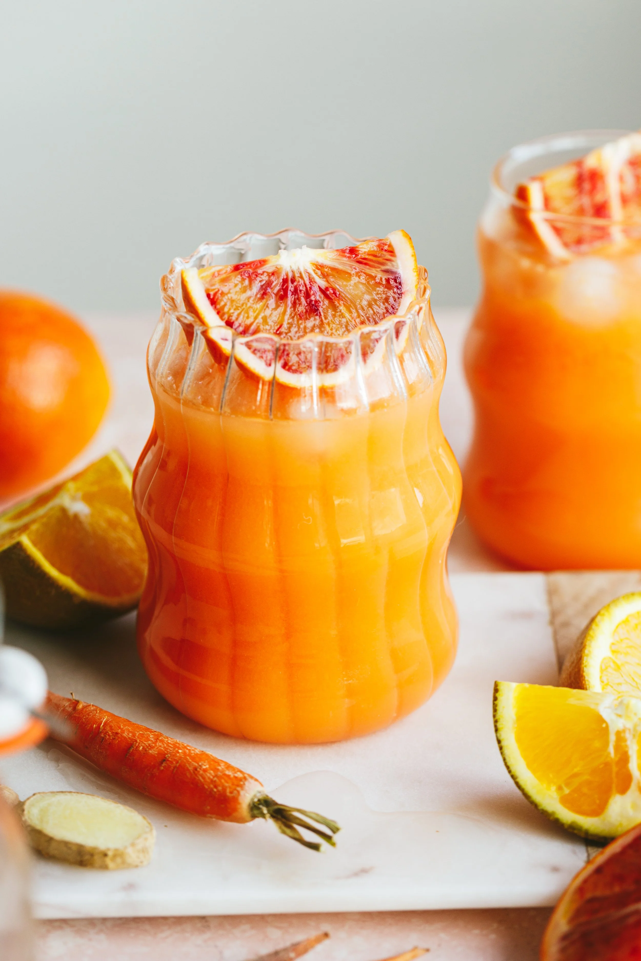 Image shows two pretty glasses full of vibrant orange juice garnished with sliced blood orange