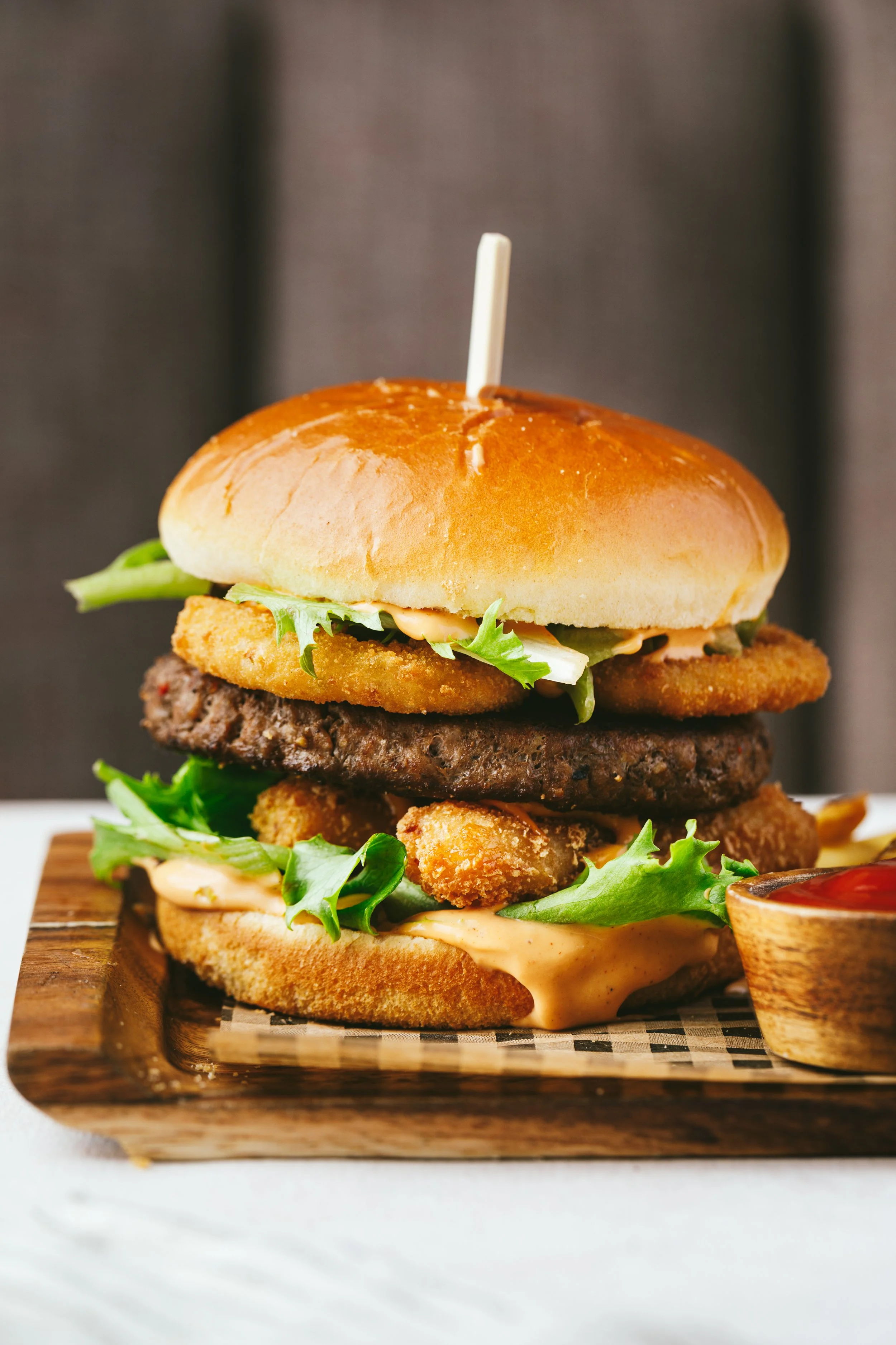 Kimberly Espinel portfolio image with a side view of a burger stacked high with garnishes and sauce spilling out of the sides..