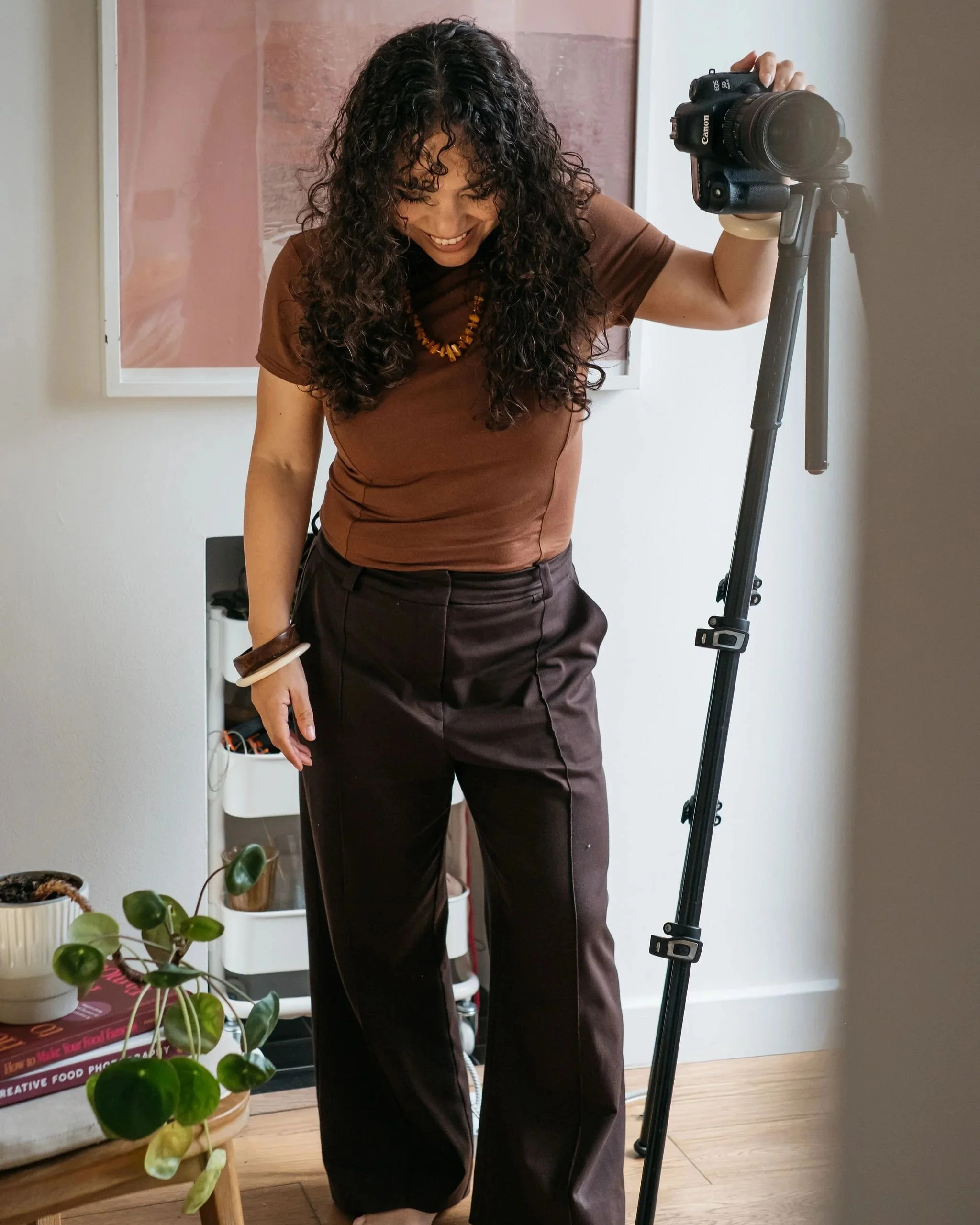 Profile image of Kimberly Espinel, creator of the Fearless Focus Mentoring programme - Kimberly is standing beside her tripod looking down and smiling, one hand on her camera mounted on the tripod.