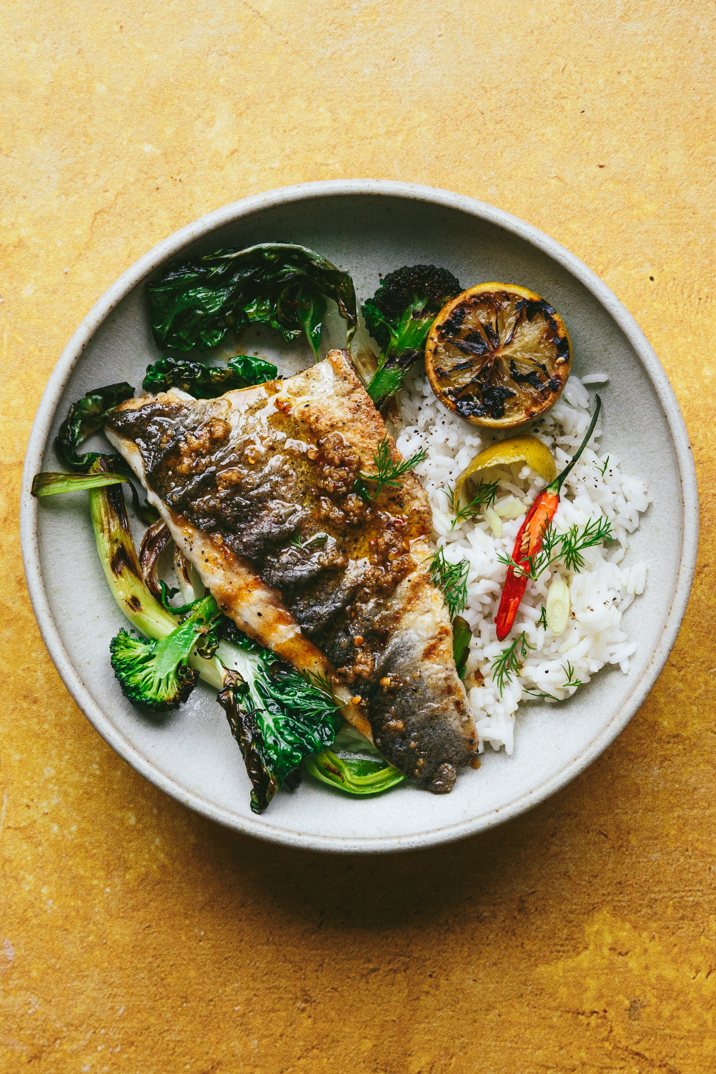Blog post image showing a dish with cooked fish on top of rice and charred vegetables