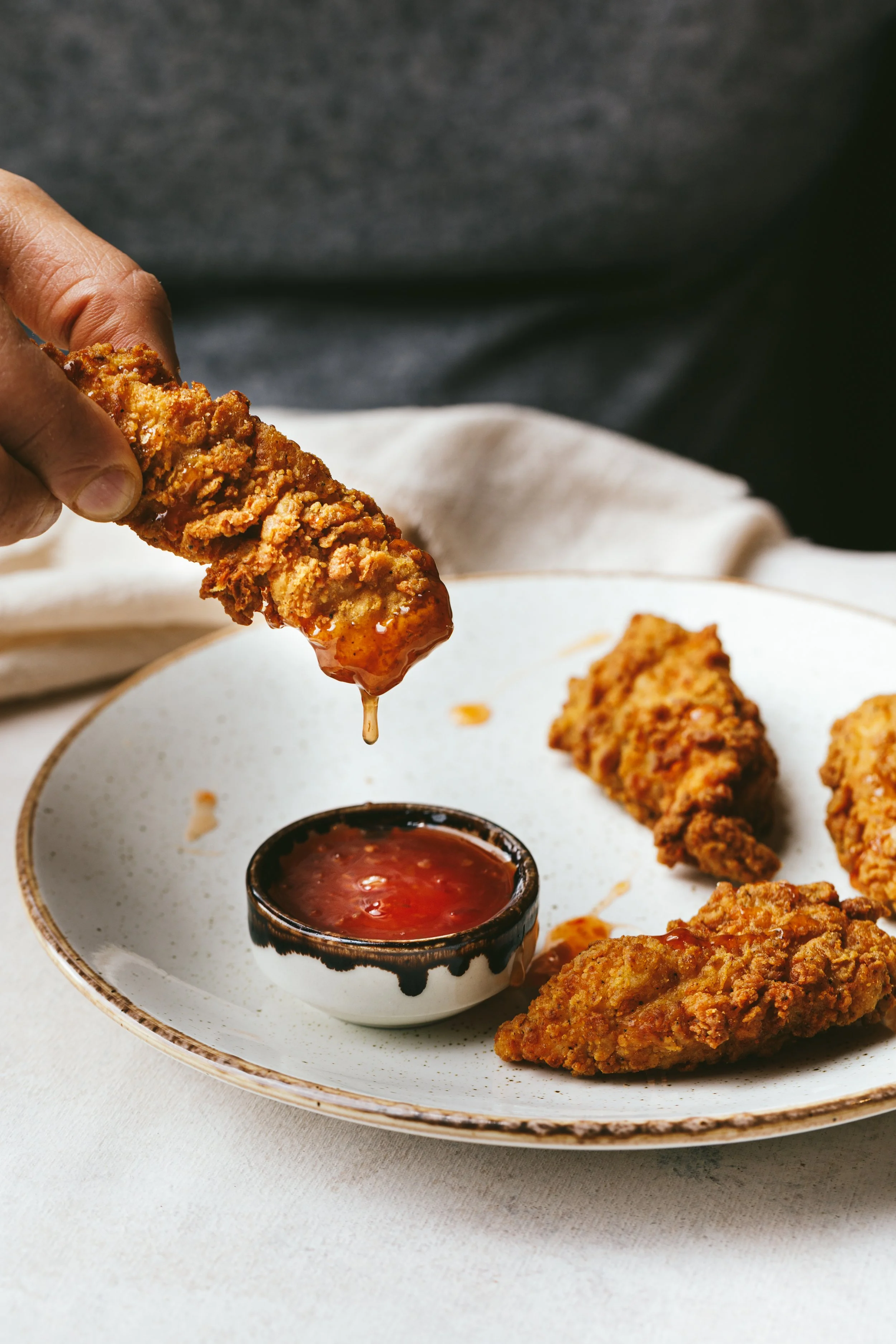 Blog post image showing a hand holding a battered strip of something tasty, being dipped into a little bowl of chilli sauce
