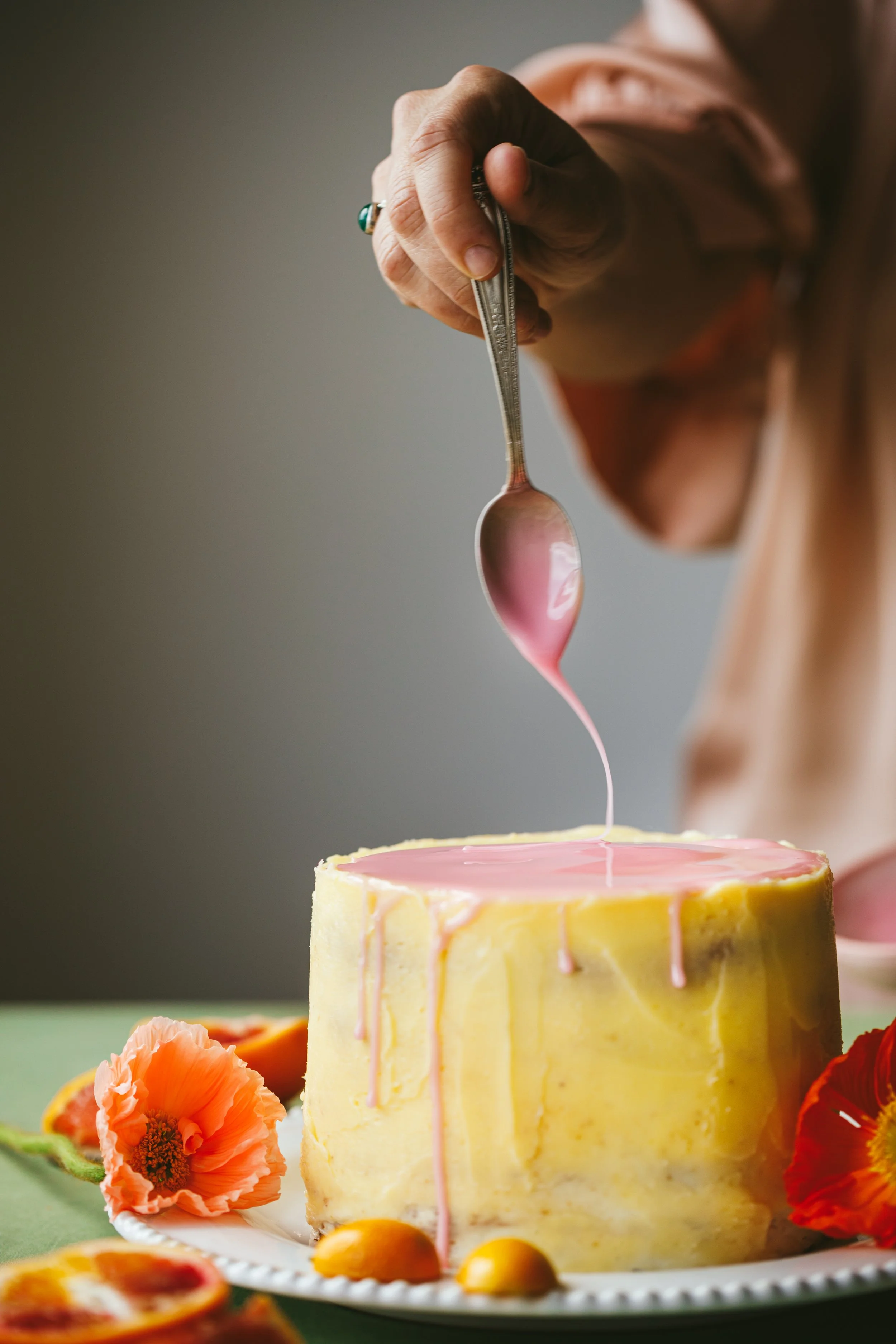 Blog post image showing a hand drizzle pink icing over a beautifully frosted yellow cake