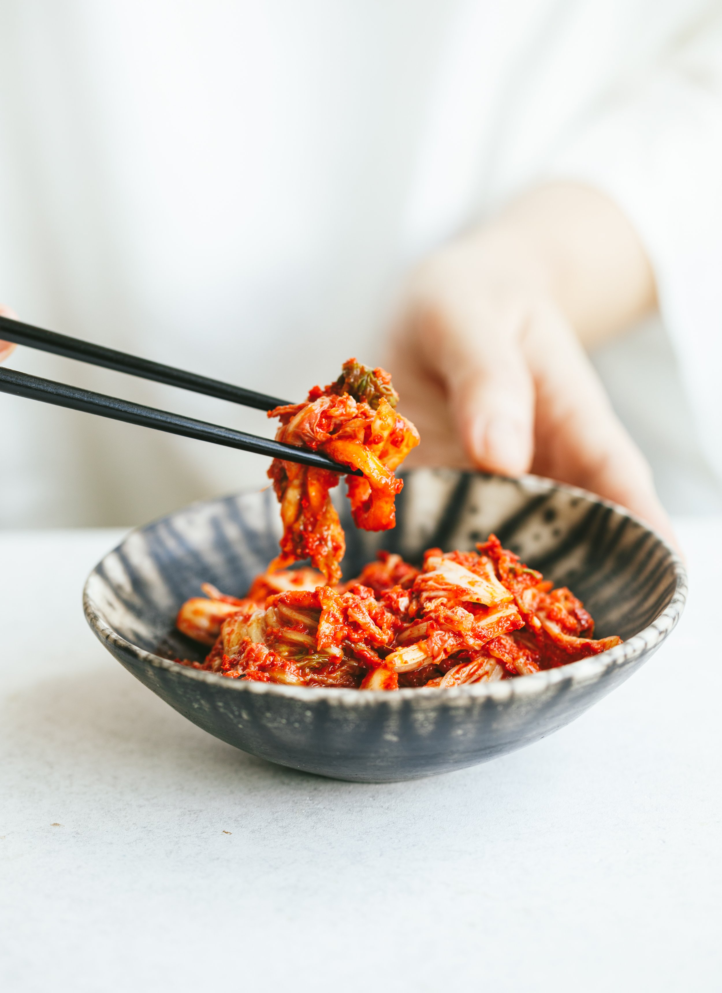Kimberly Espinel portfolio image showing a small bowl of kimchi, while chopsticks are holding some of it up.