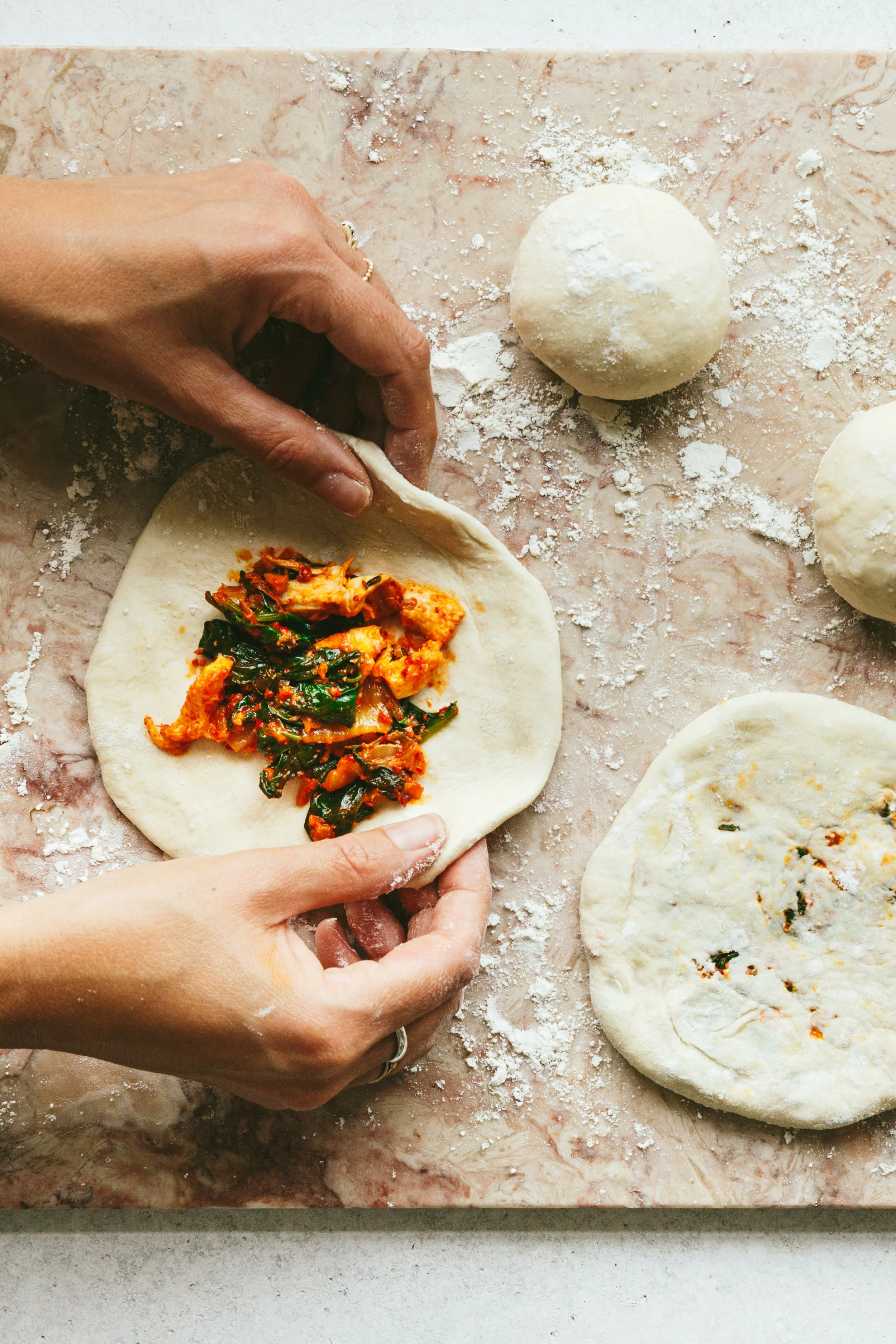 Kimberly Espinel portfolio image showing hands folding a round piece of dough with some kimchi in the centre.