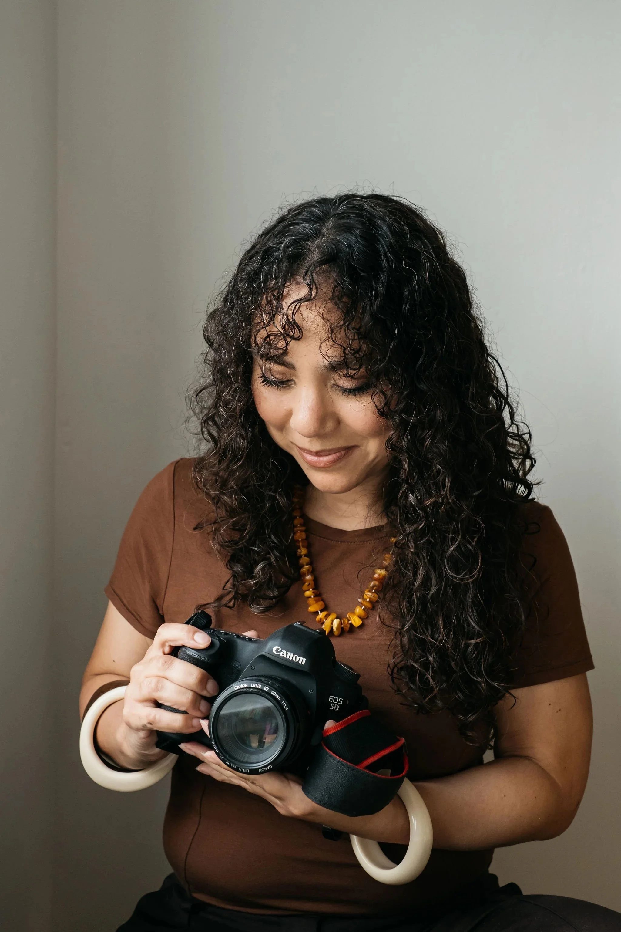 Profile image of Kimberly Espinel, author, podcaster and food content creator and educator. Kimberly is looking down towards a camera she is holding in her hands.