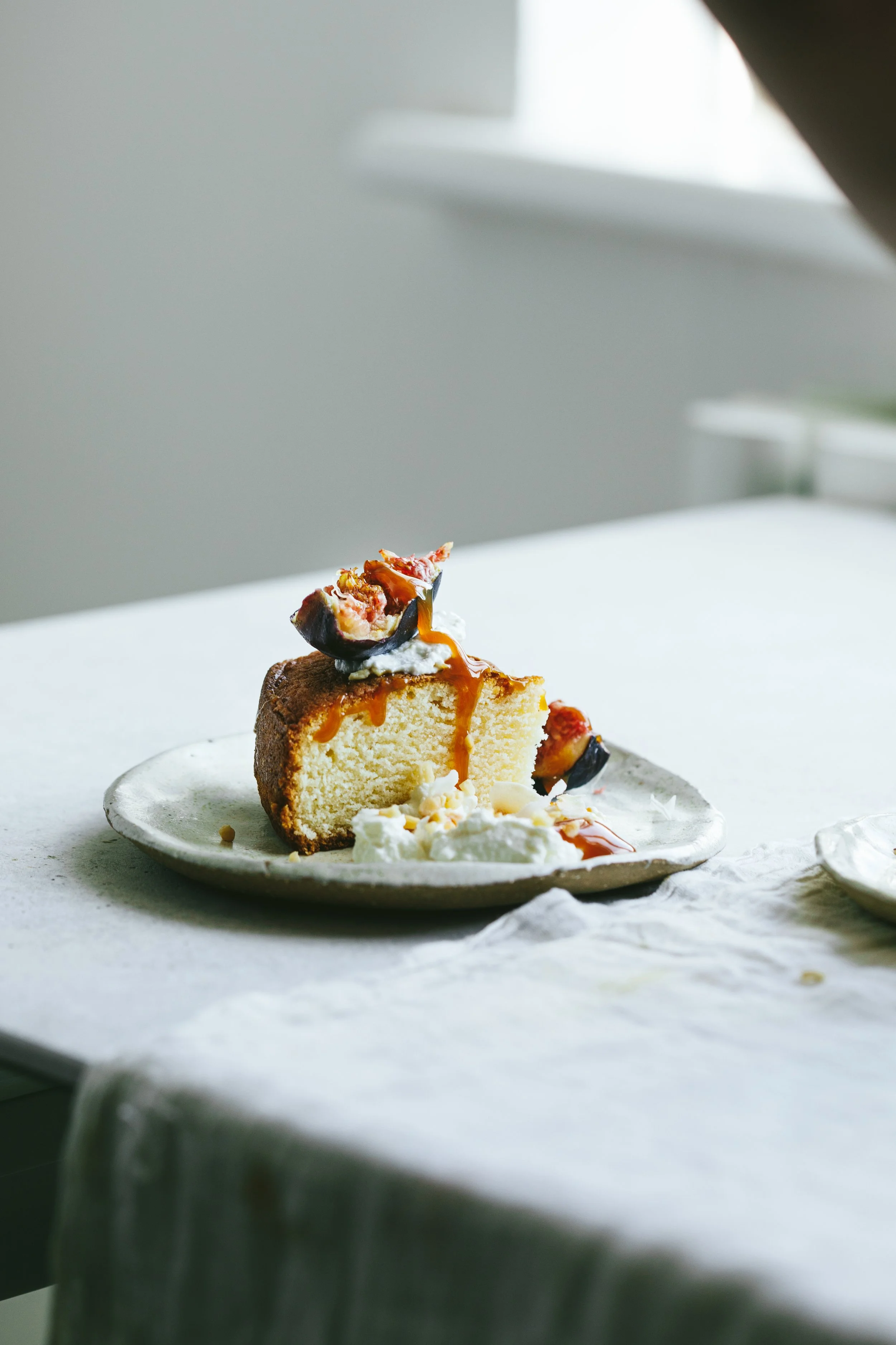 Blog post image with light background showing a piece of cake on a plate with some fig on top and cream on the side