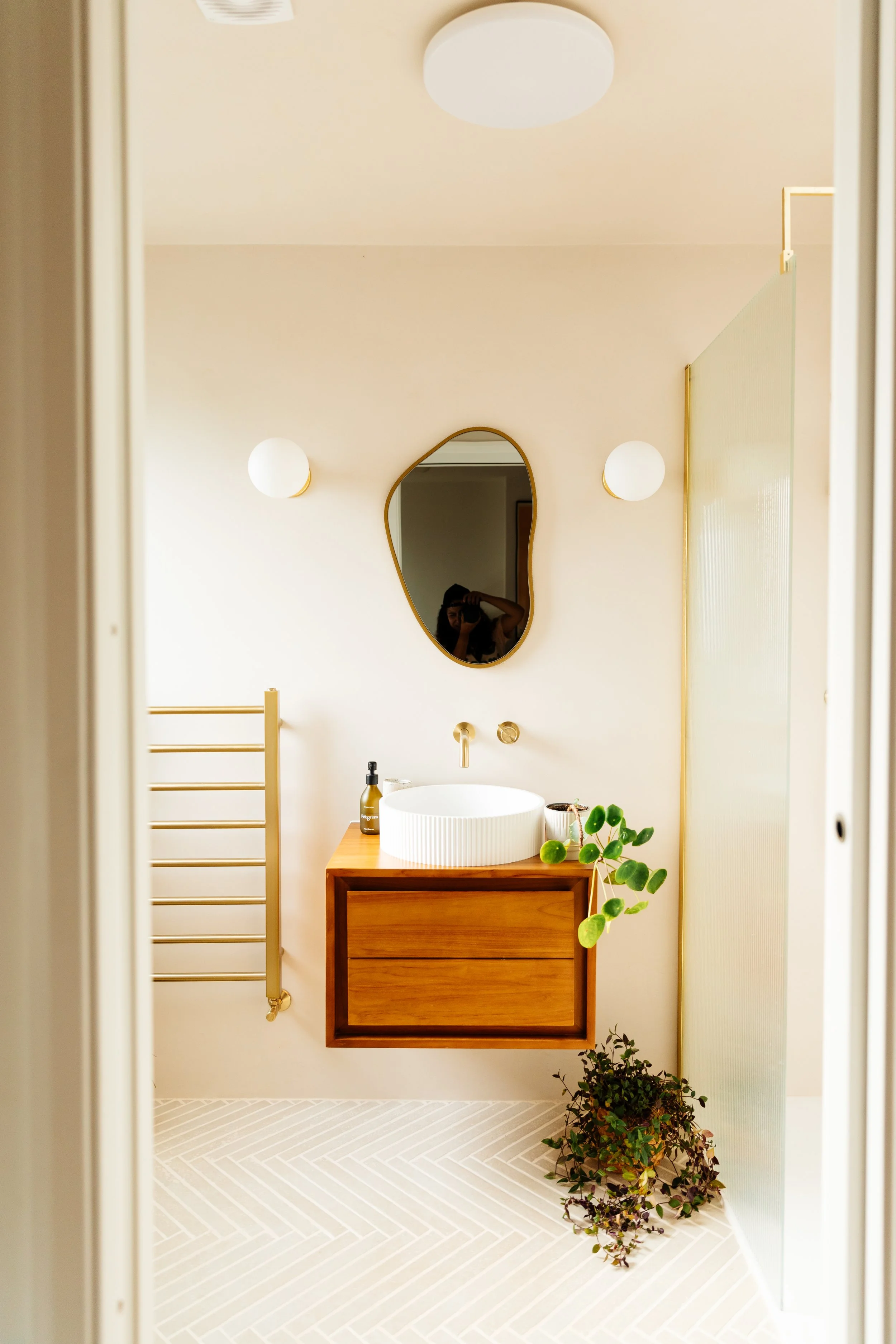 Blog post image showing the bathroom sink and vanity unit, the mirror and part of the heated towel rack. Two plants are positioned near the vanity unit