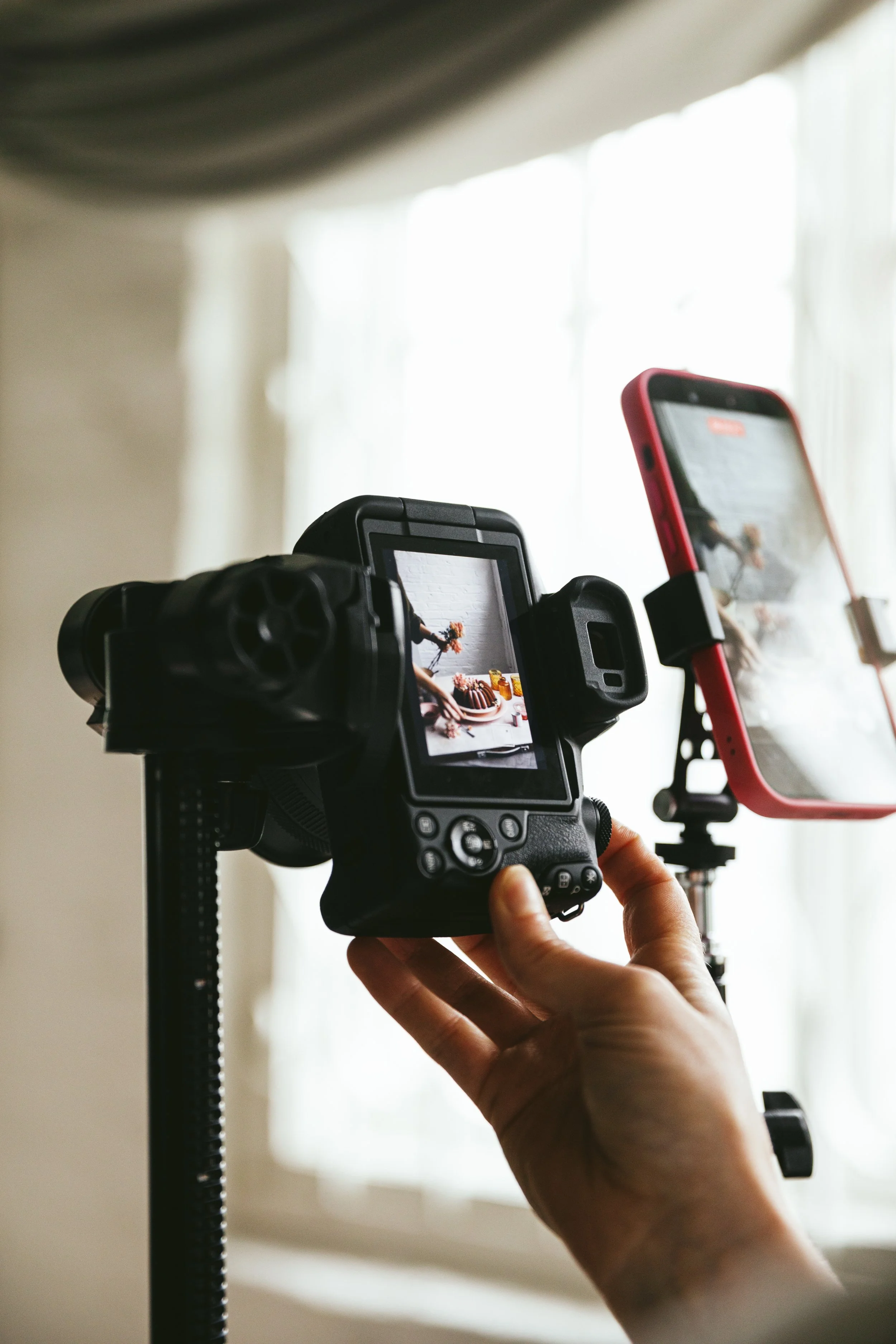 Blog post image showing a hand holding a camera set up on a tripod, aiming at a food scene