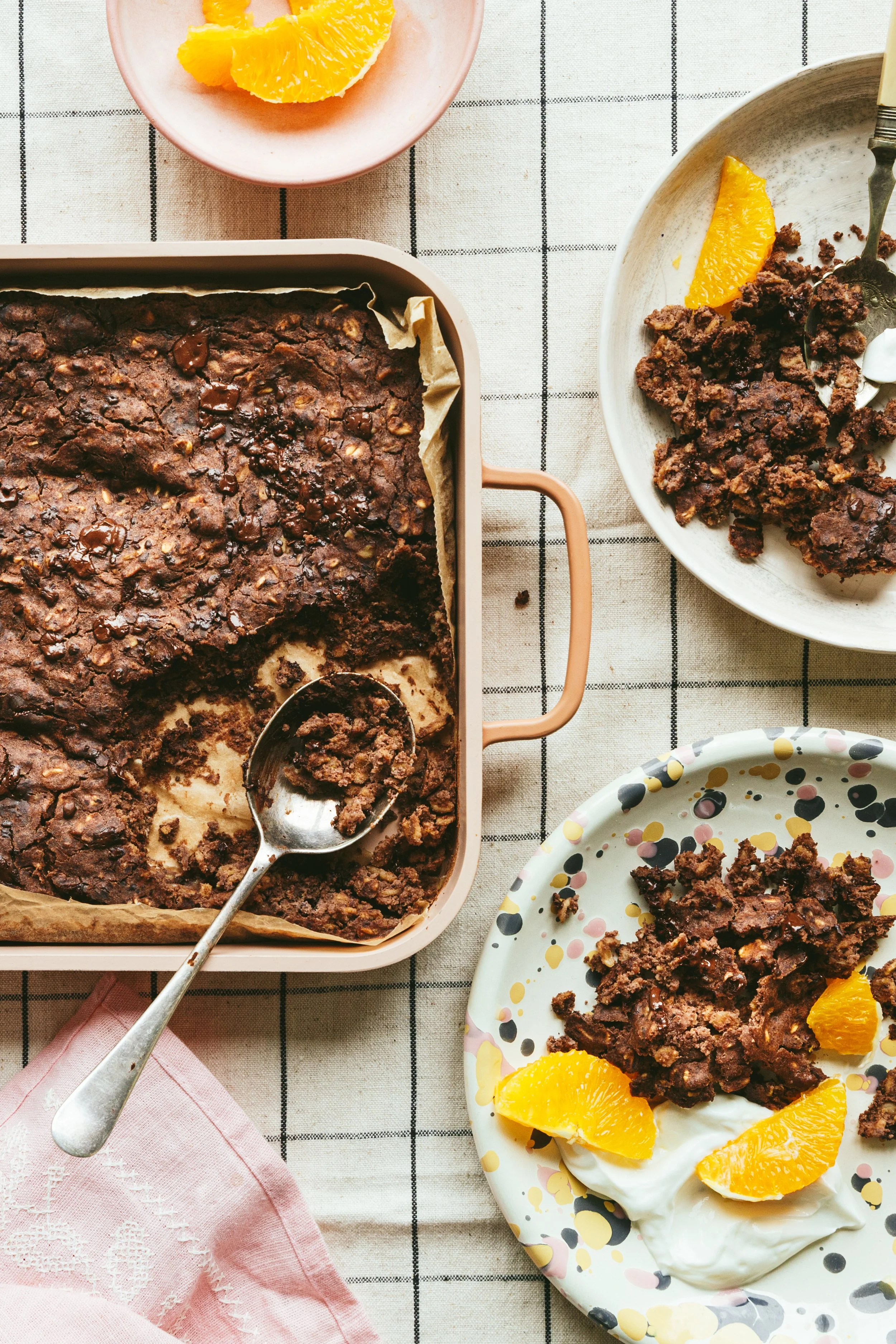 Kimbely Espinel portfolio image showing a baking tin with baked chocolate oatmeal, placed beside a dish with a serving of the oats, some yogurt and slices of orange on the side.