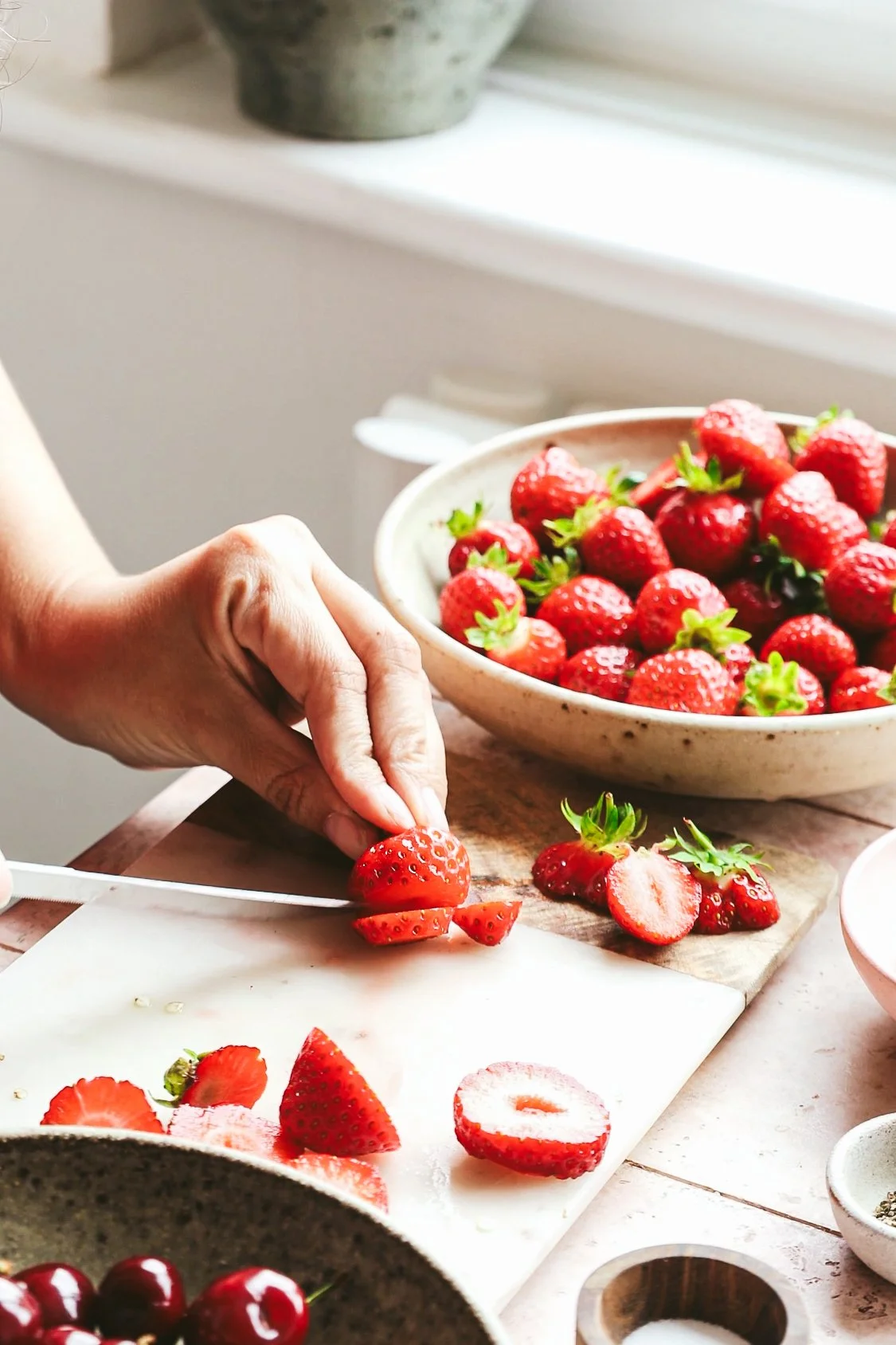 Blog post image showing hands slicing strawberries, a bowl of juicy looking strawberries at the side