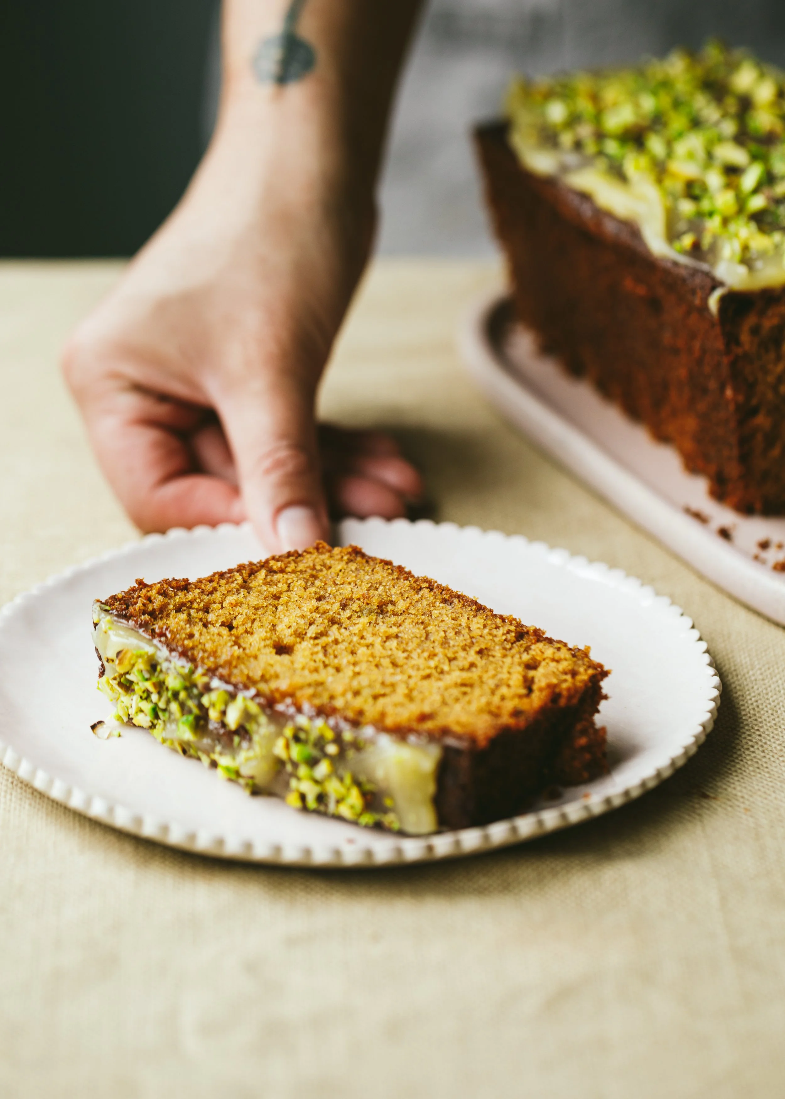 Kimberly Espinel portfolio image showing a hand reaching for a ceramic plate with a slice of pistachio loaf cake