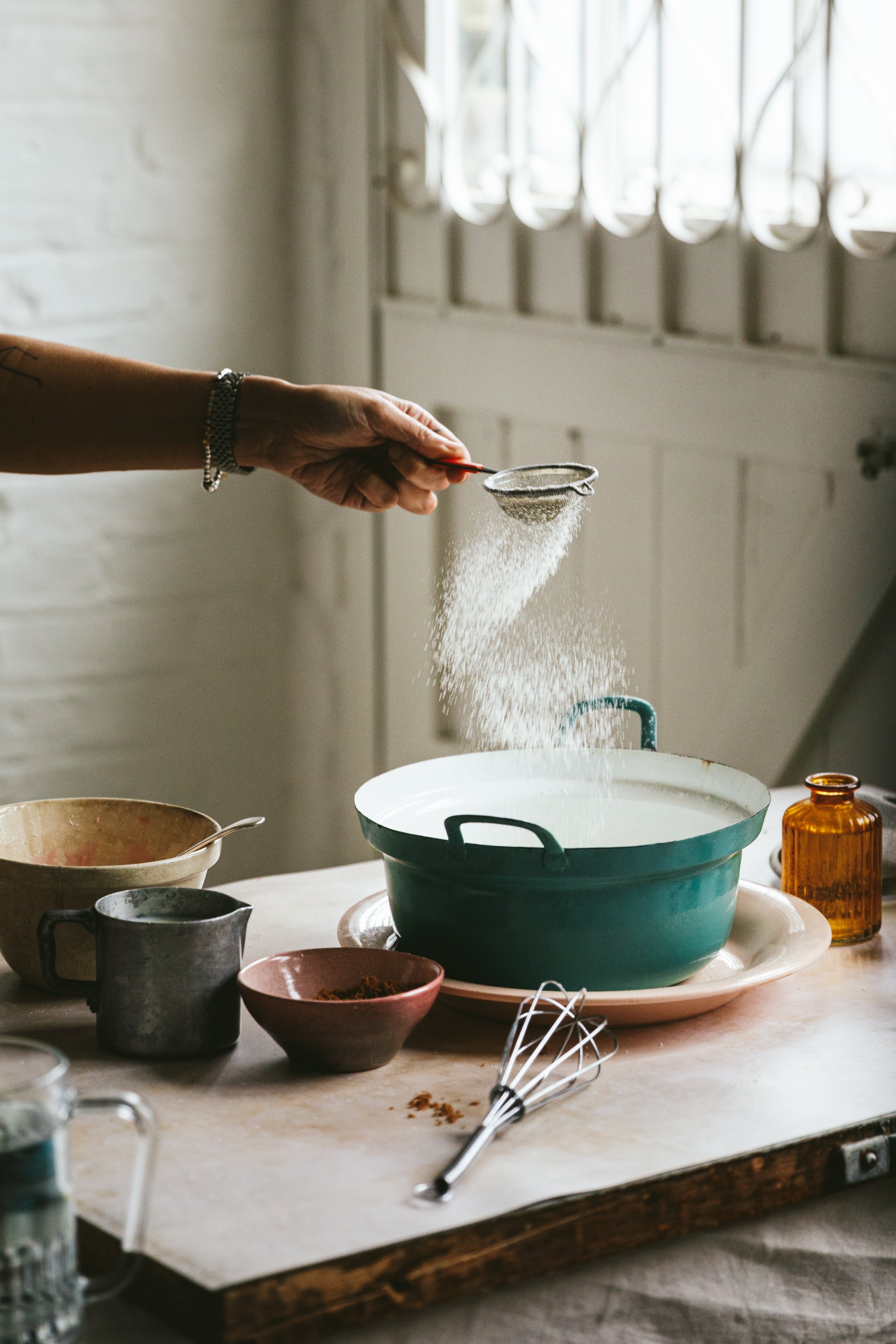 Blog post image showing a hand sprinkling icing sugar into a bowl with a tea strainer