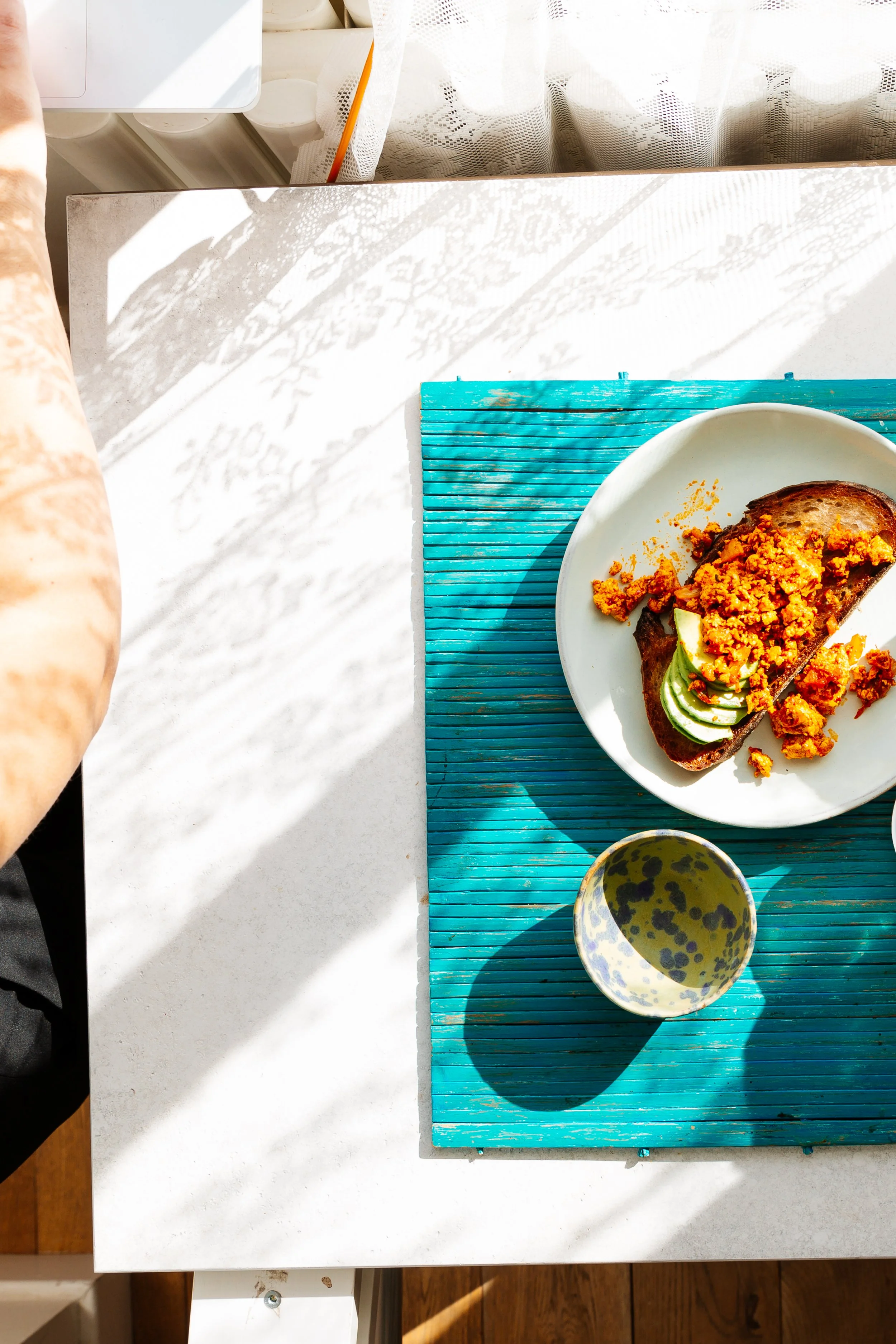 Blog post image showing a plate of food on a brightly coloured place mat, sitting on a white surface with dappled light reflected on it from a window.