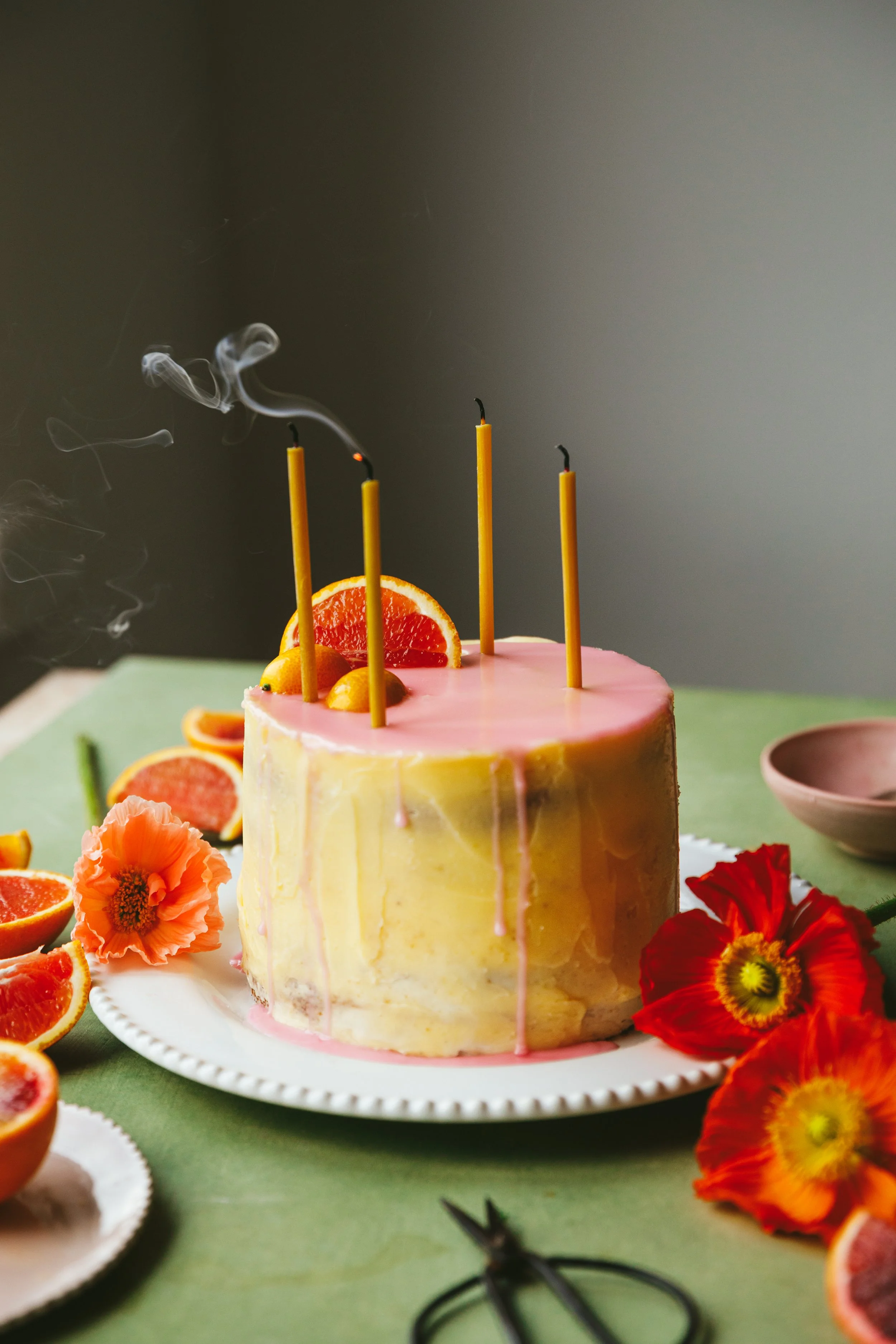 London videography workshop blog post image showing a layered cake with pretty yellow and pink icing, long candles still smoking, and garnish of orange slices and flowers