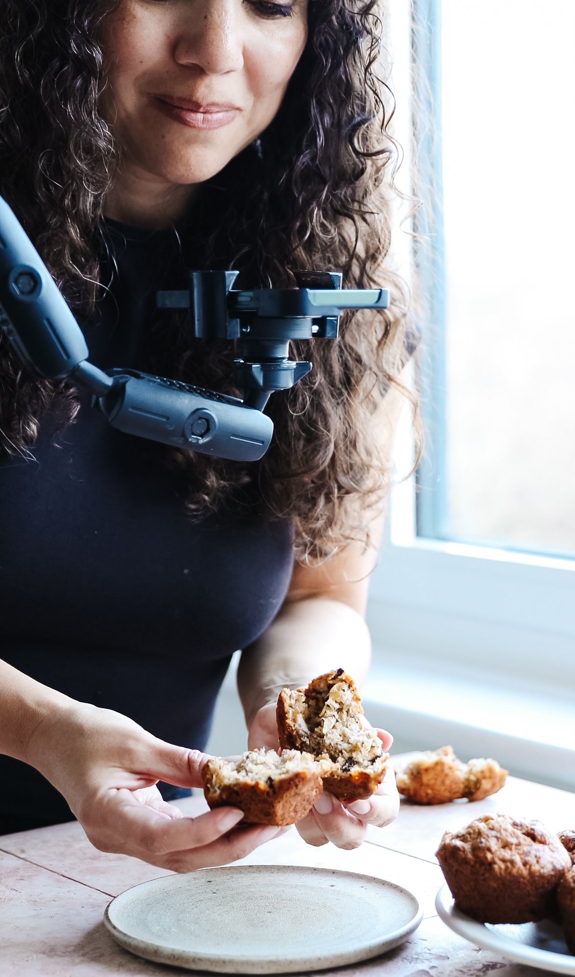 Blog post image showing author Kimberly holding a halved muffin under a camera on a holder, during filming of a recipe reel
