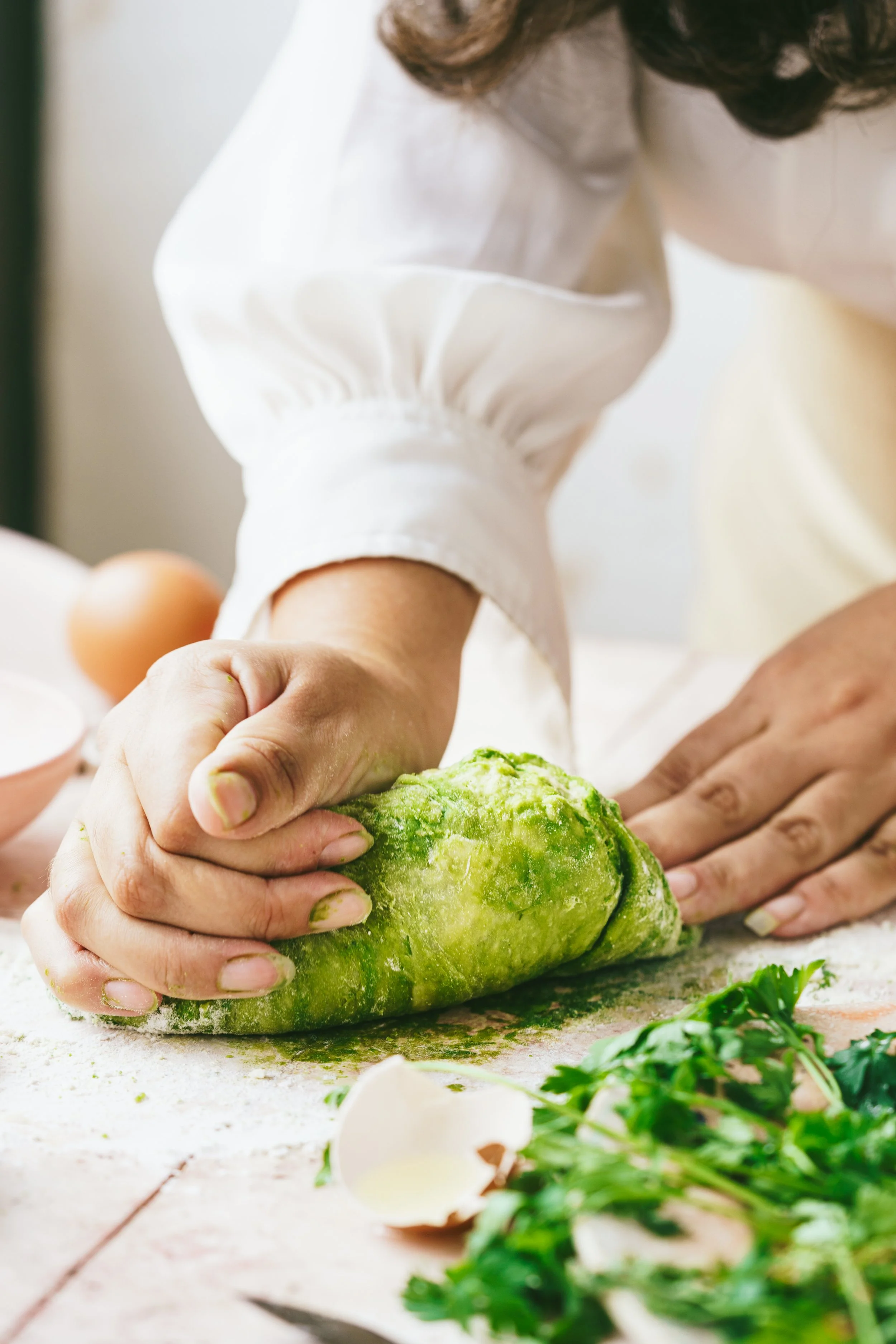 Image shows hands kneading dough that has herbs incorporated giving it a vibrant green colour