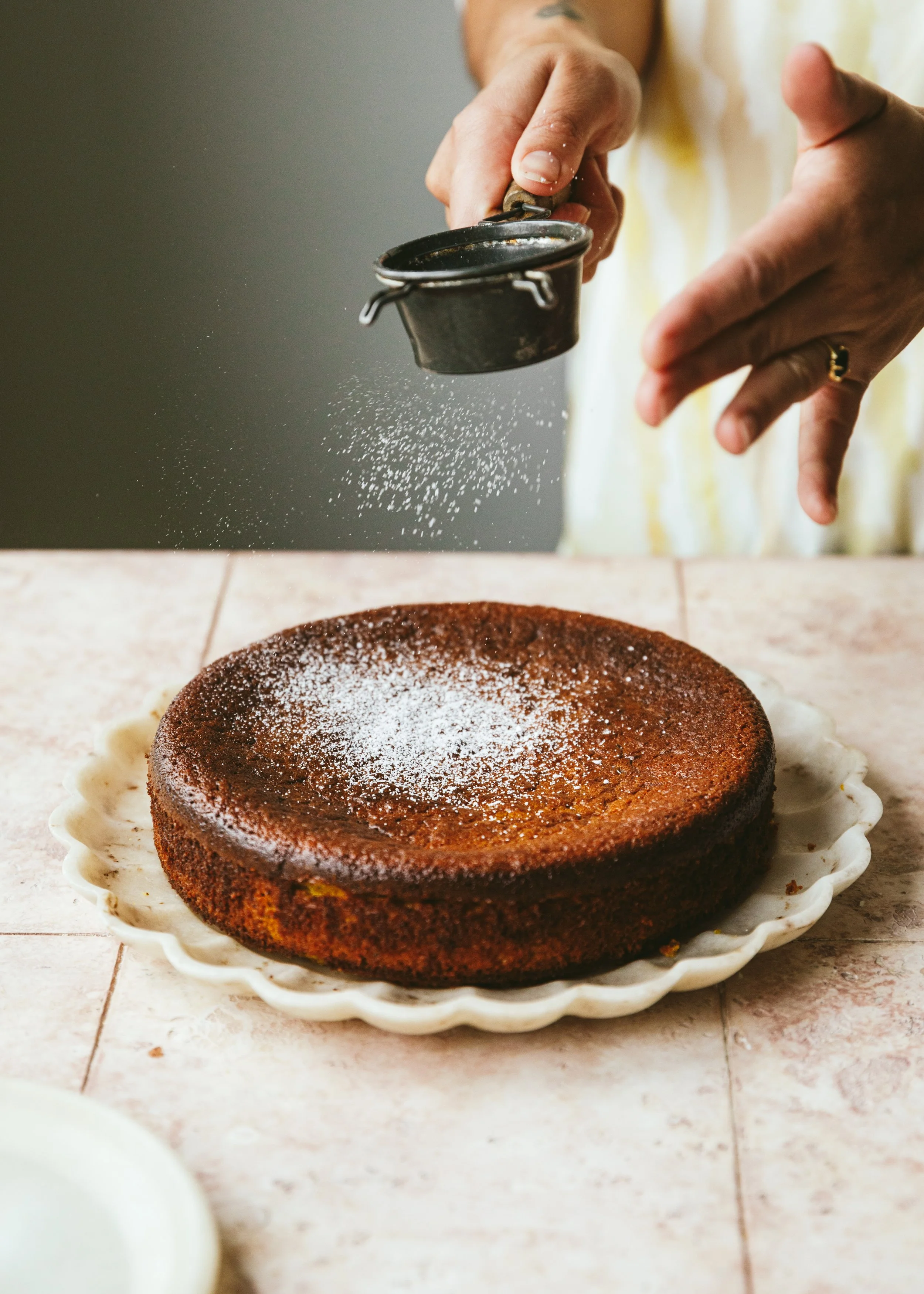 Kimberly Espinel portfolio image showing hands dusting a cake with icing sugar