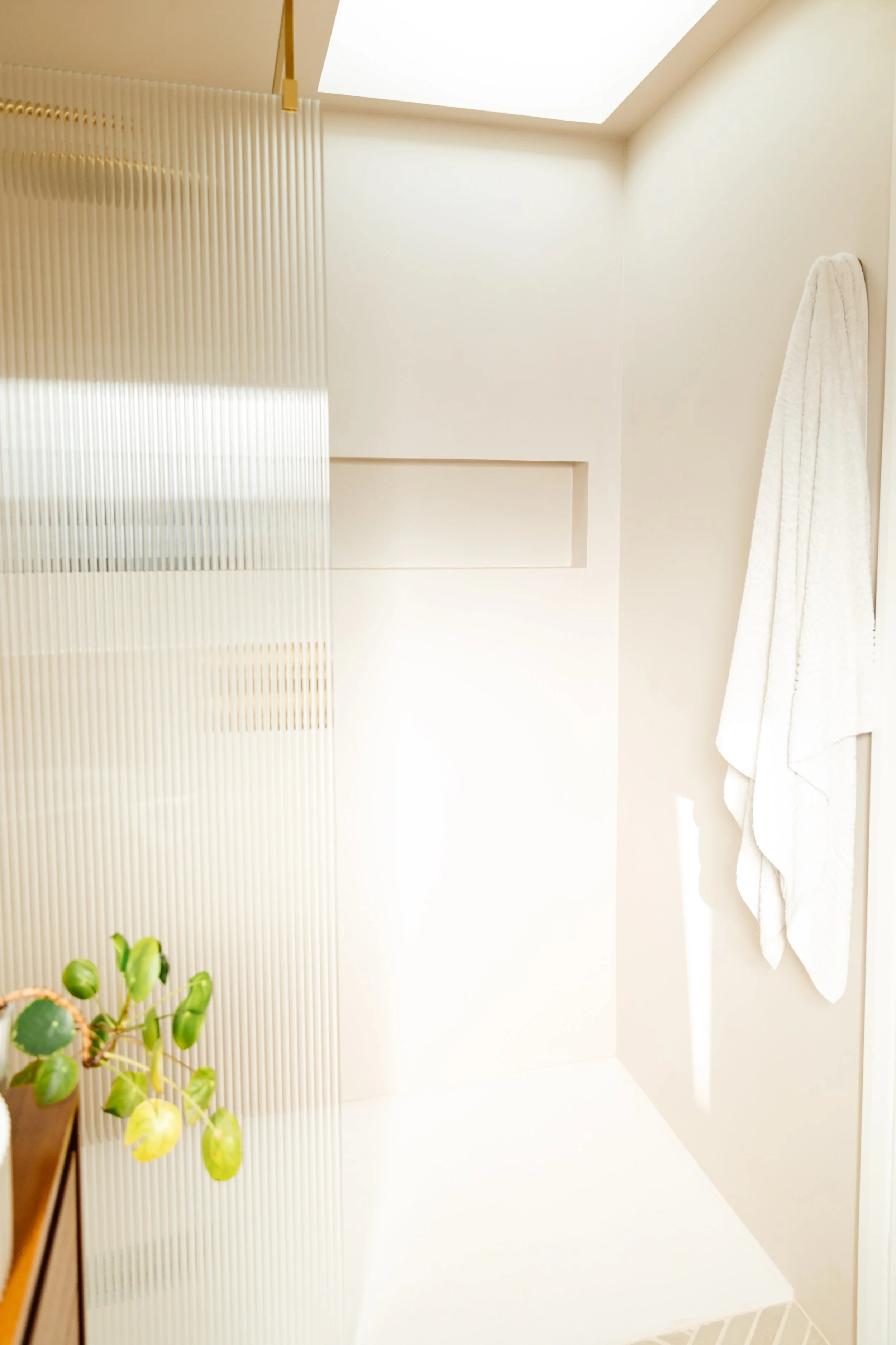 Blog post image showing a bright shower corner with reeded glass partition. A green plant and bath towel are visible on each side of the image
