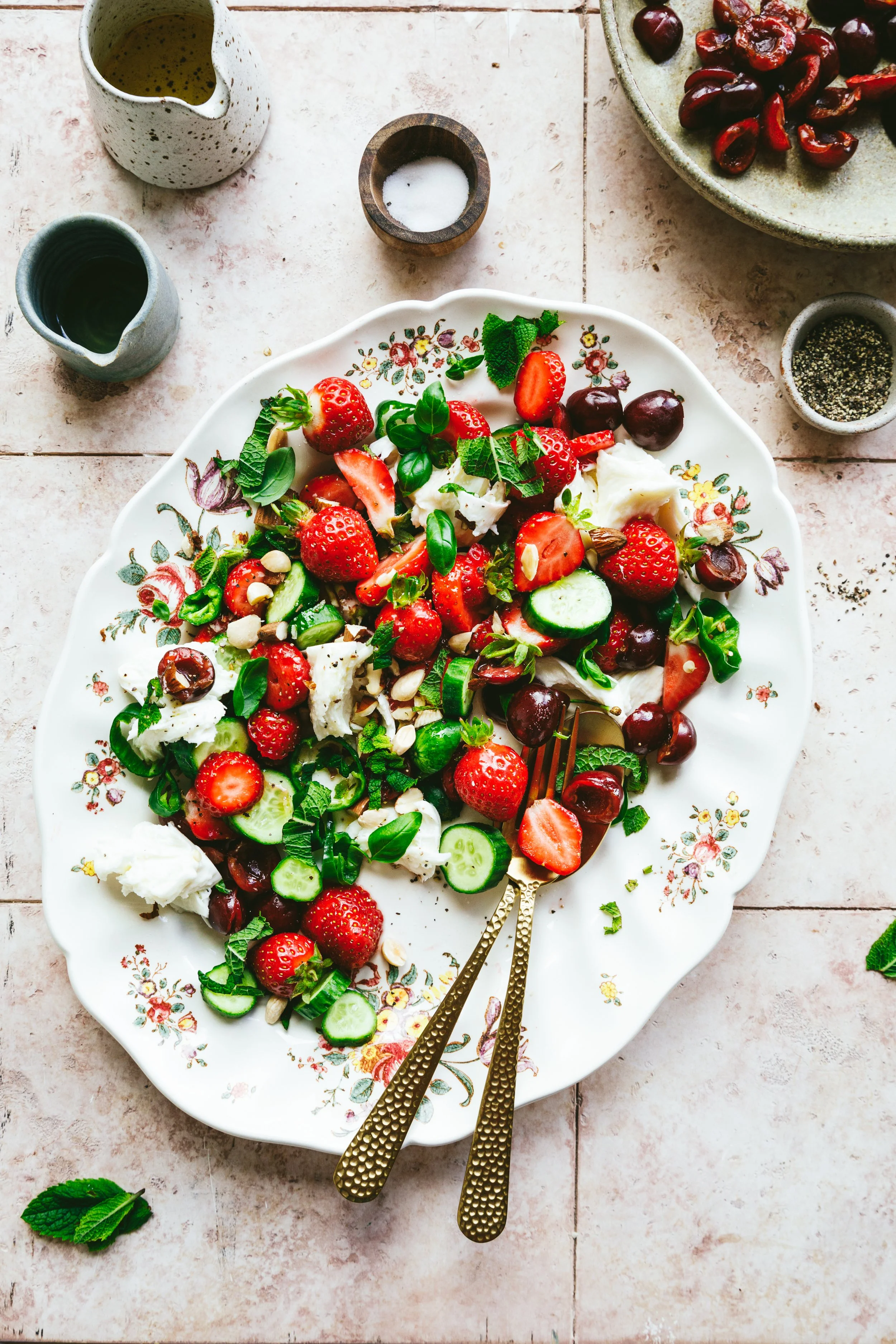 Blog post image showing a pretty platter with strawberry, cherry, pepper, cucumber and mozzarella salad garnished with herbs and almonds.