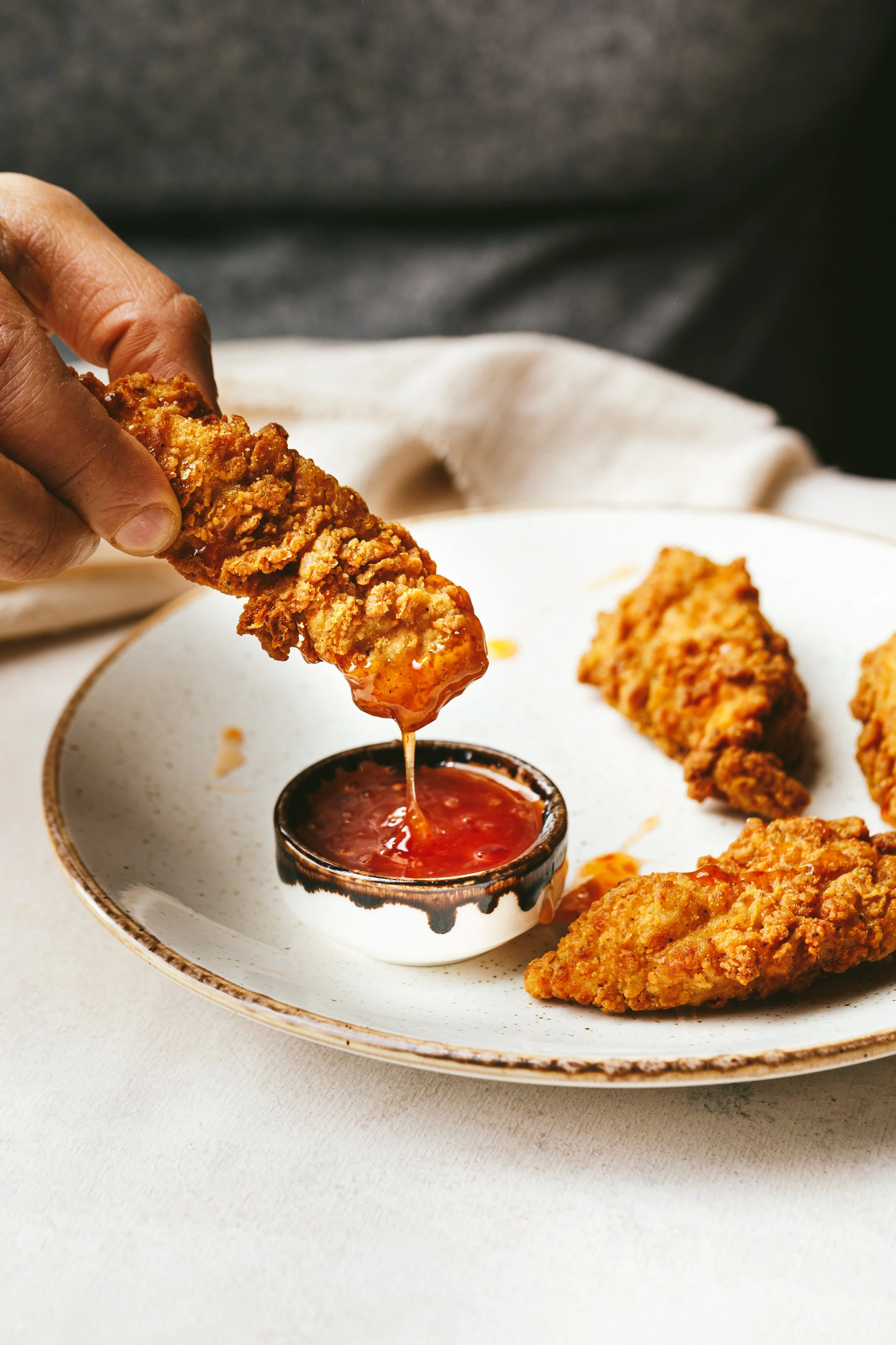 Kimberly Espinel portfolio image showing a hand dipping a nugget into some sticky red sauce.