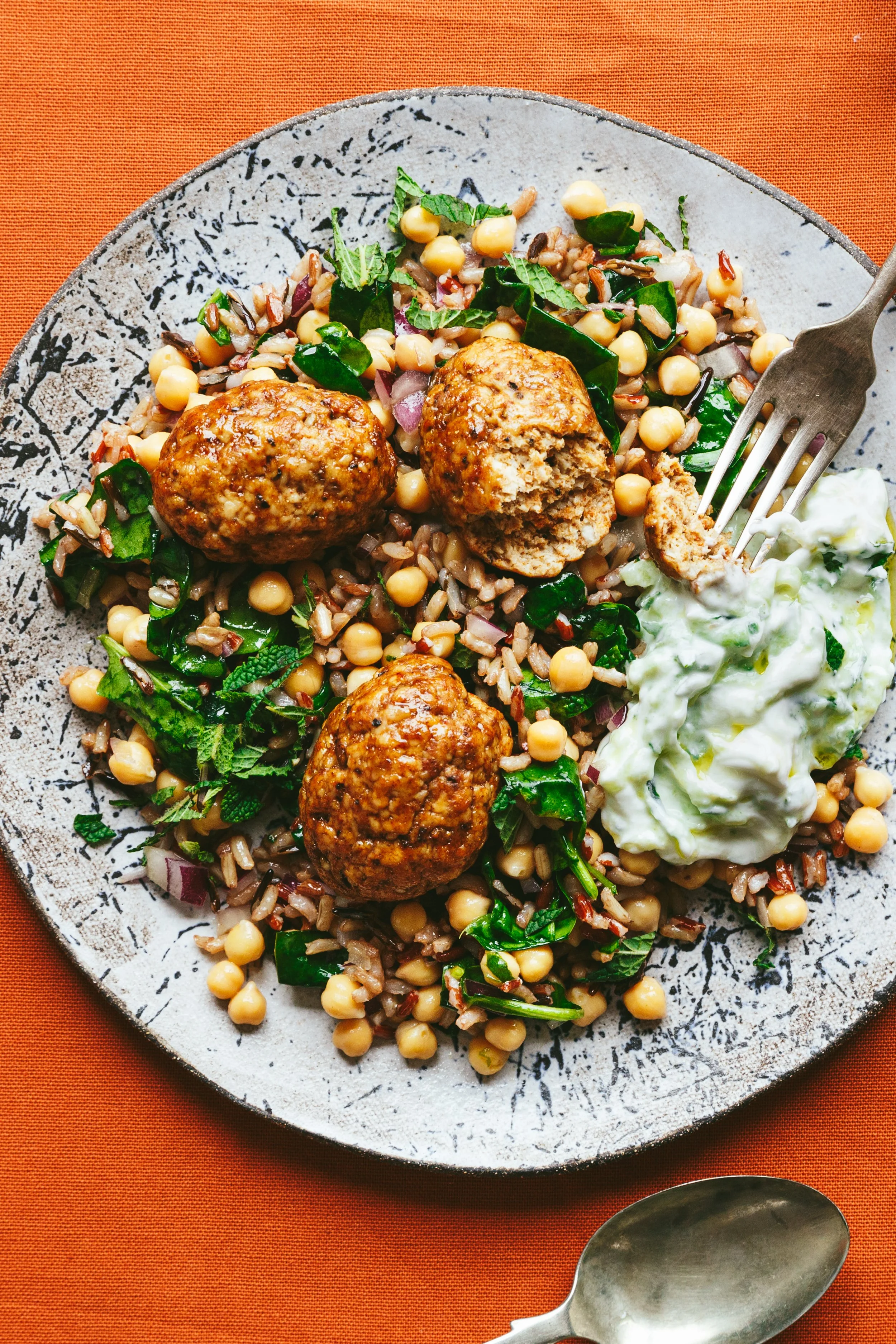 Kimberly Espinel portfolio image showing a close up view of a dish with grains and legumes, chopped greens, "meatballs" on top and tzatziki on the side..