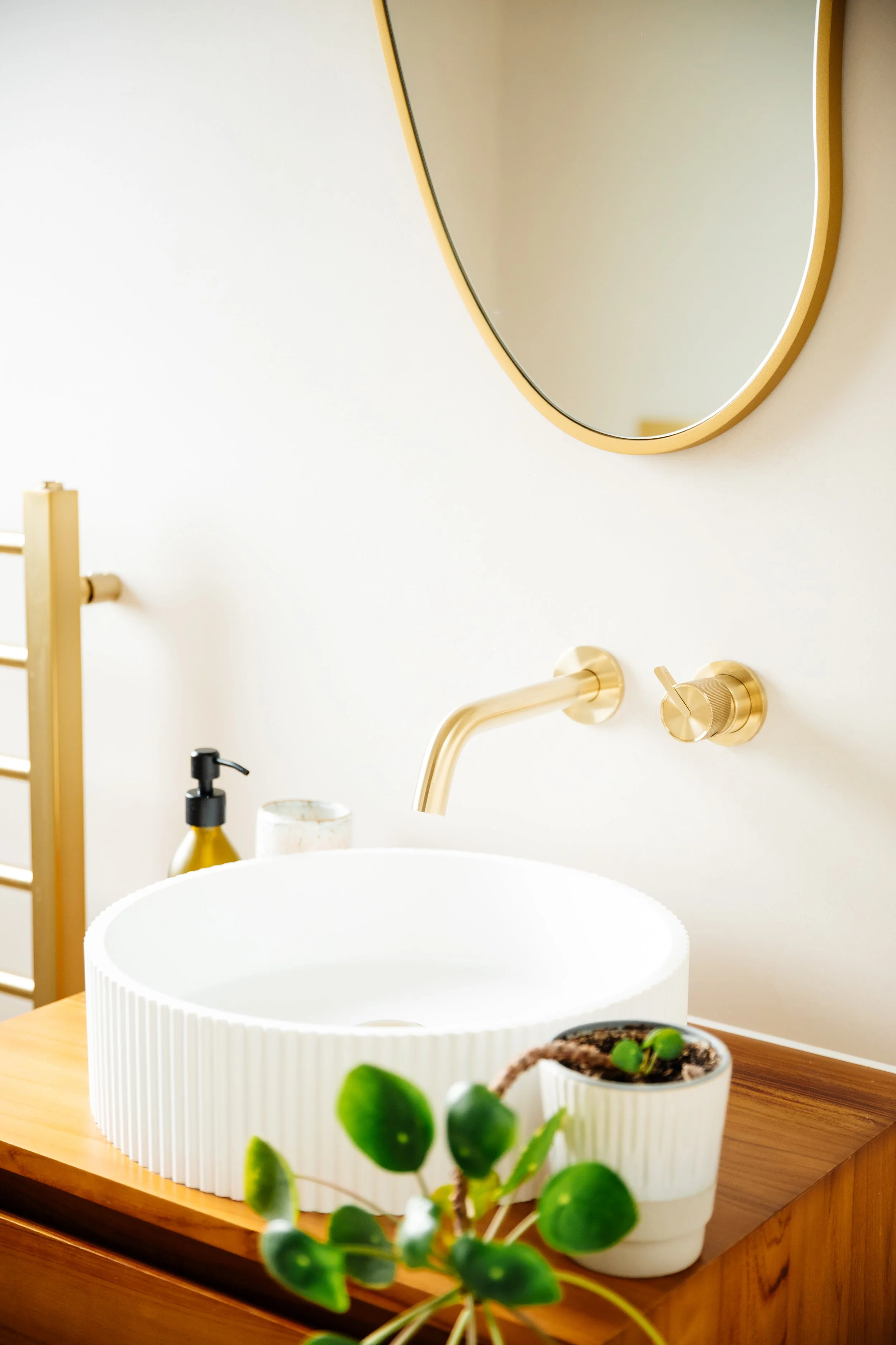 Blog post image showing an elegant bathroom sink and mirror, a plant positioned on the vanity unit next to the sink.