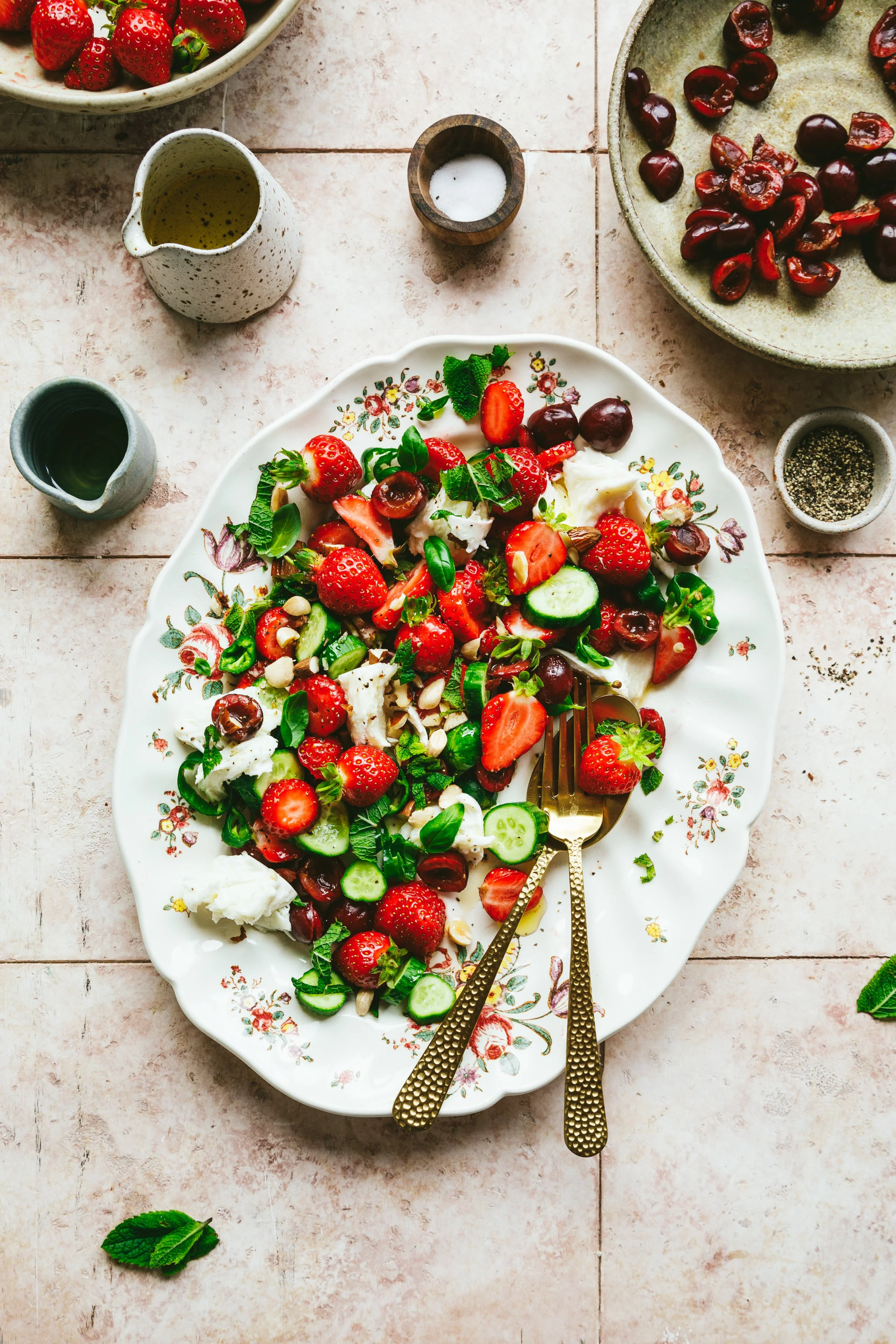 Blog post image showing a pretty platter with strawberry, cherry, pepper, cucumber and mozzarella salad garnished with herbs and almonds.