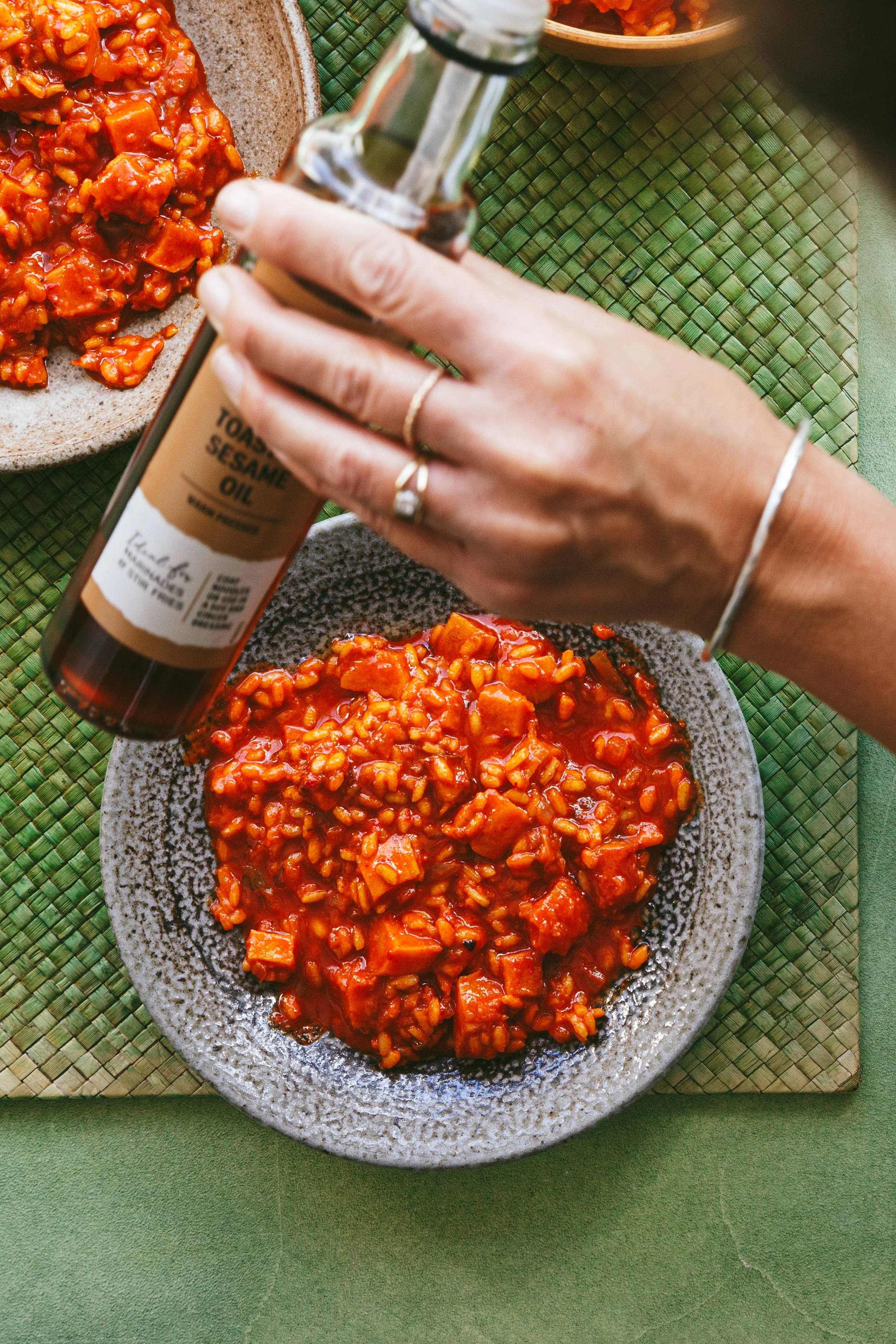 Blog post image showing hands holding a bottle of sesame oil over a plate of delicious looking rice in a red sauce