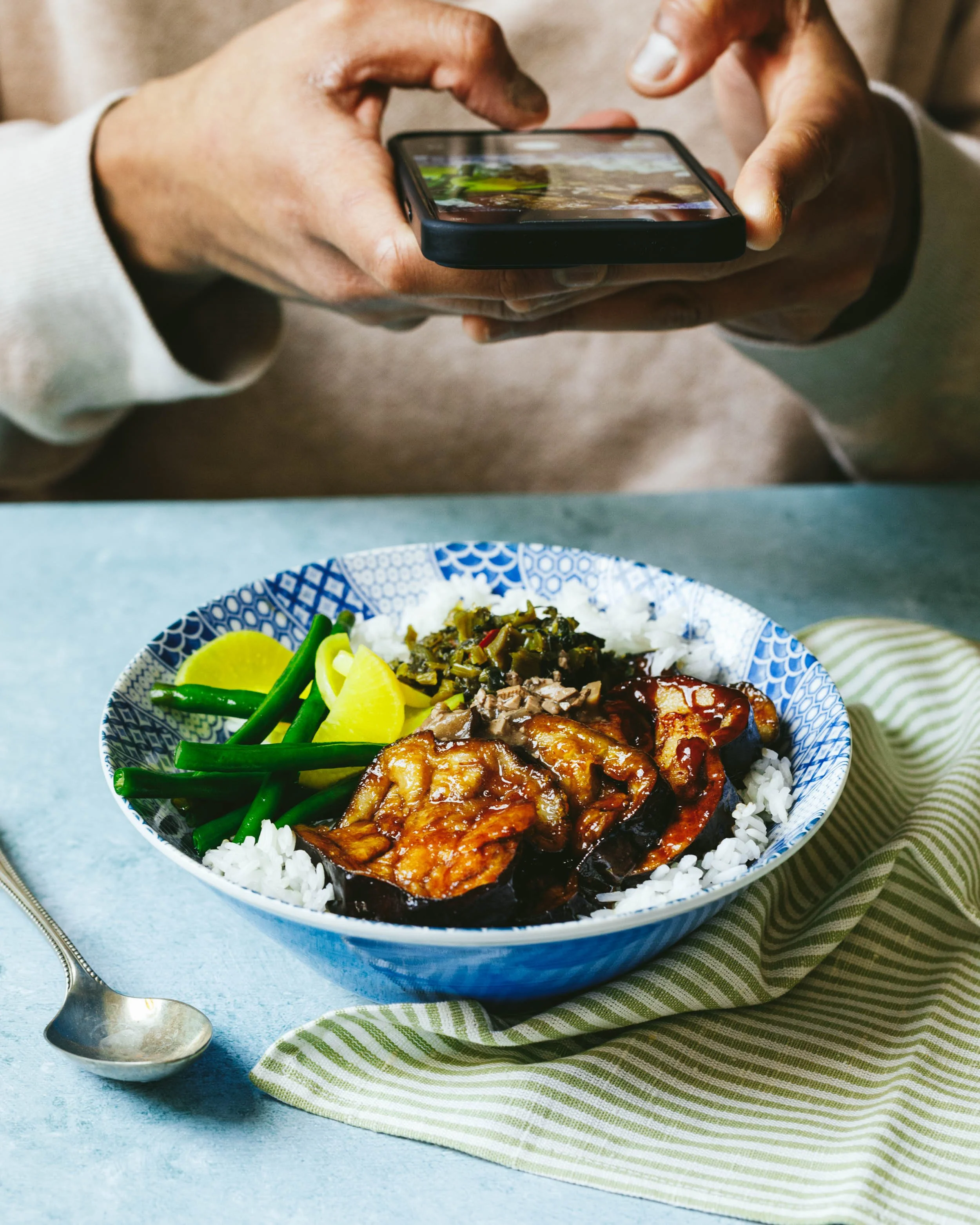 Image shows hands using a smart phone to take a picture of a bowl of food