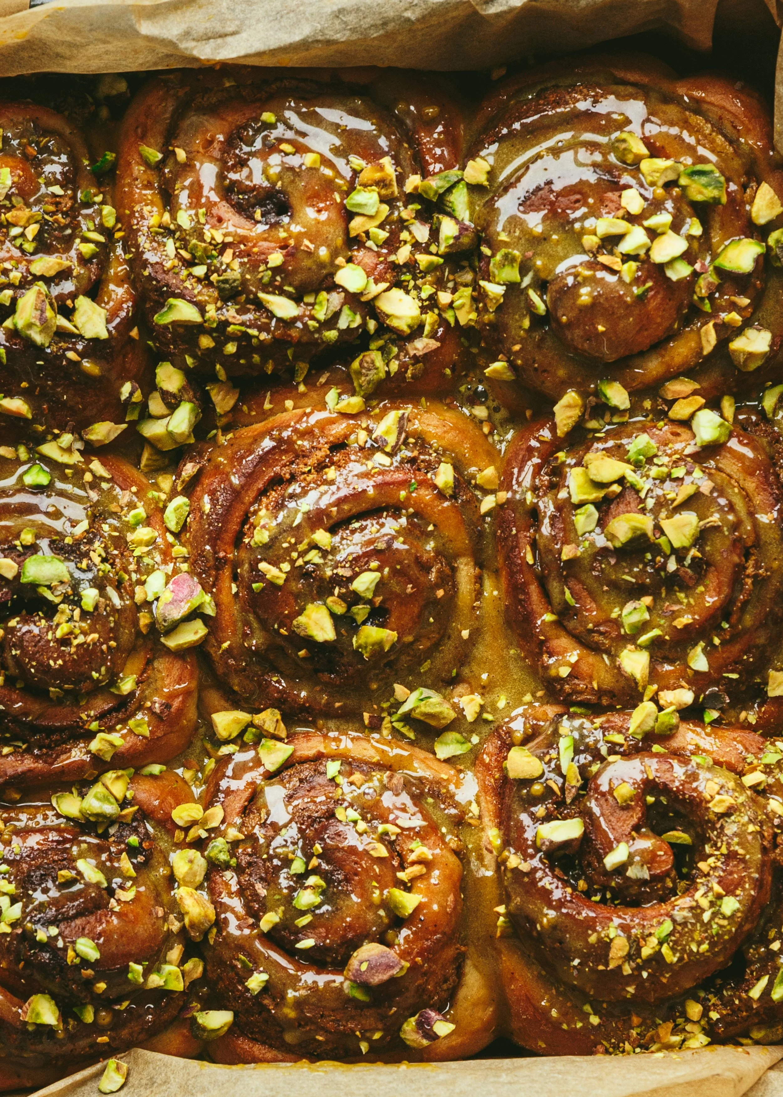 Kimberly Espinel portfolio image showing close up of cinnamon rolls in a pan covered in glaze and chopped pistachios