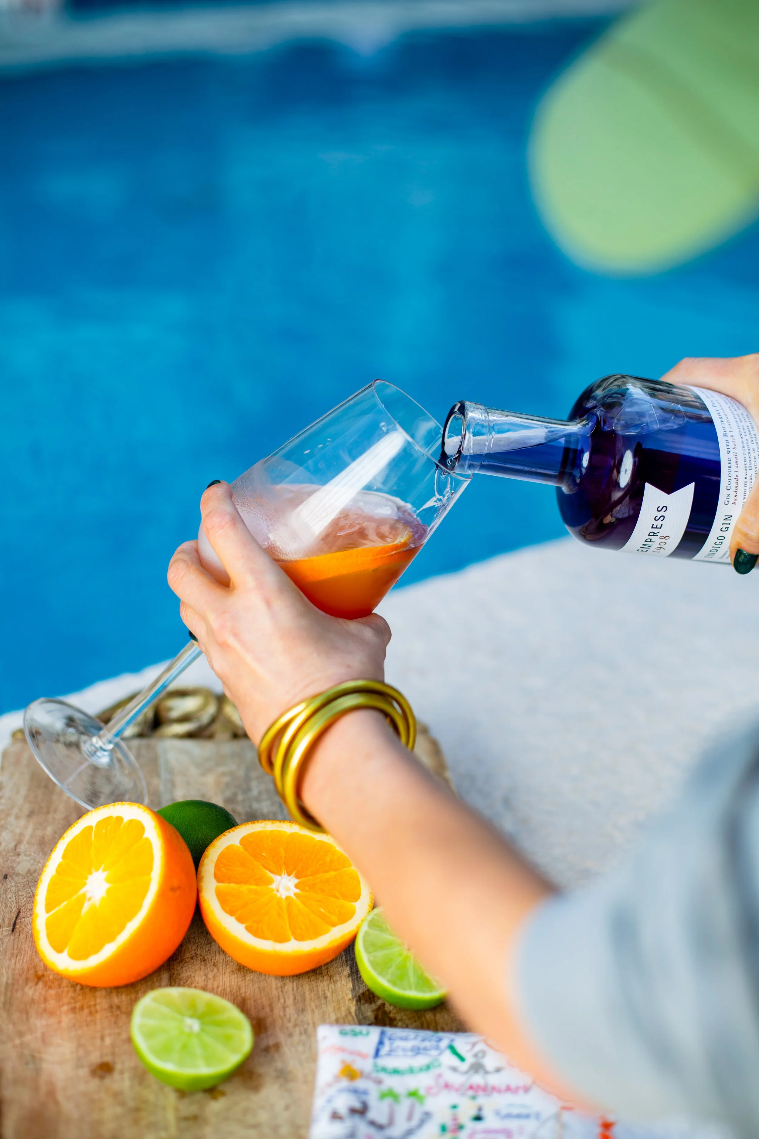 Hands pouring a colorful drink over fresh citrus, vibrant product and brand photography scene