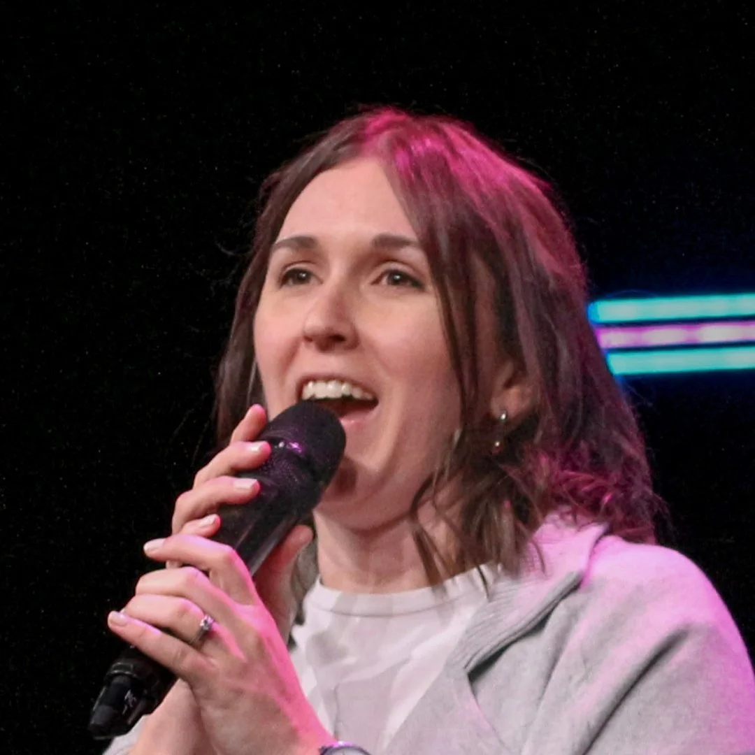 Woman singing into a microphone on a stage with colorful lights