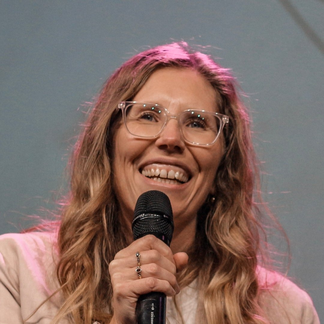 Smiling woman wearing glasses and holding a microphone on stage