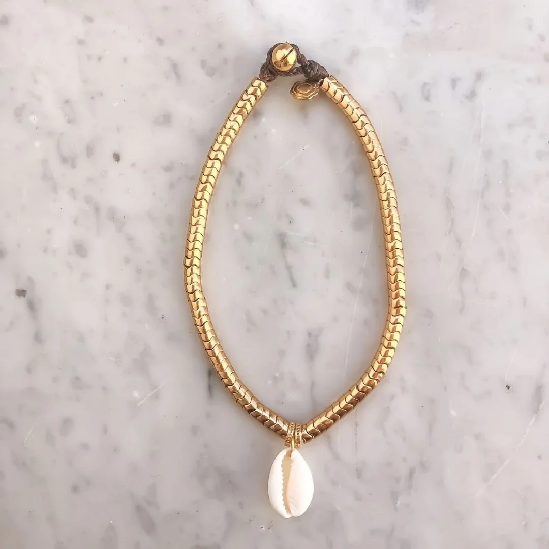 Collier en or avec pendentif en coquillage, posé sur une surface en marbre.