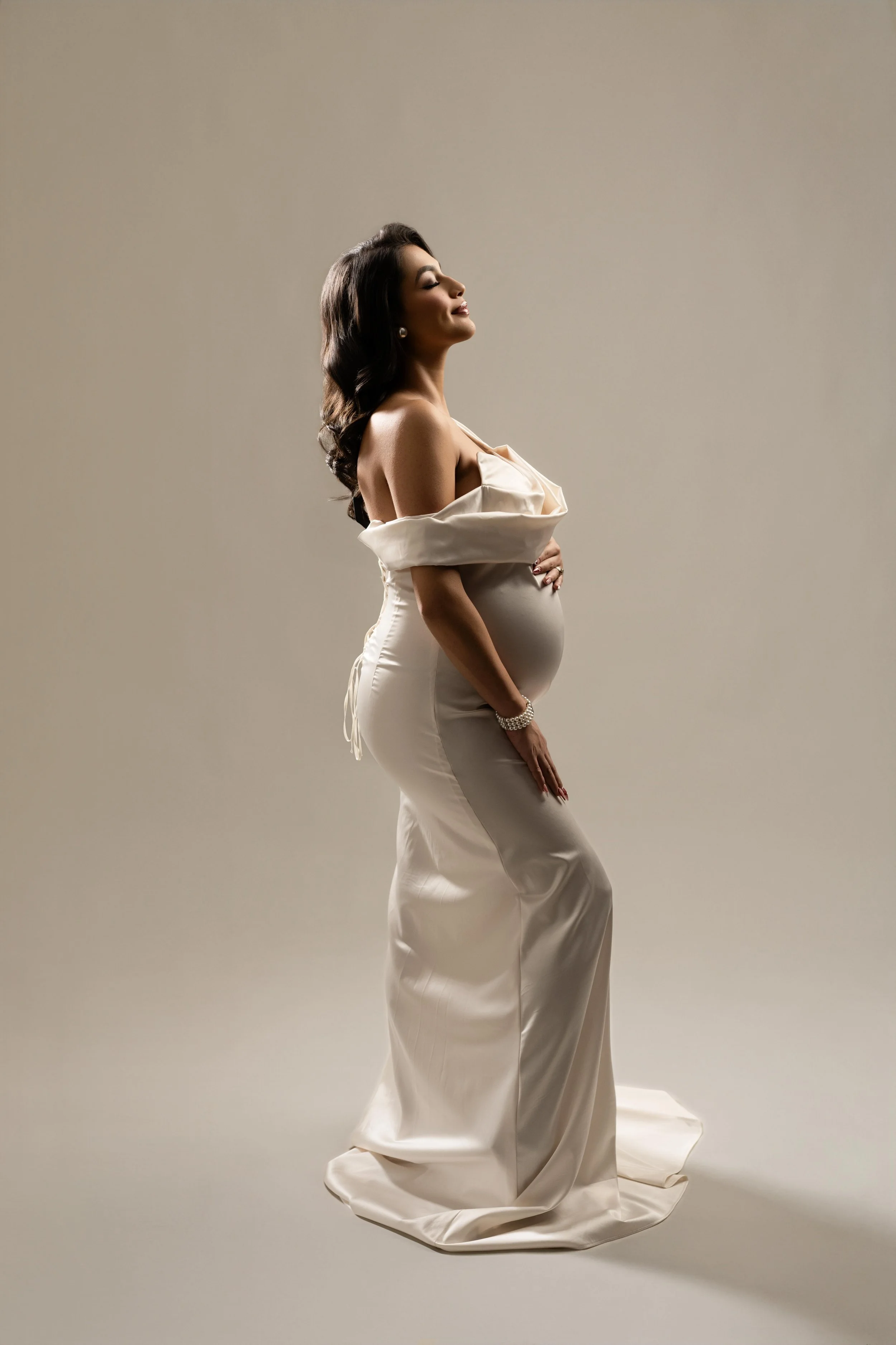 Elegant maternity portrait in a flowing white gown with soft studio lighting, photographed in Dallas.