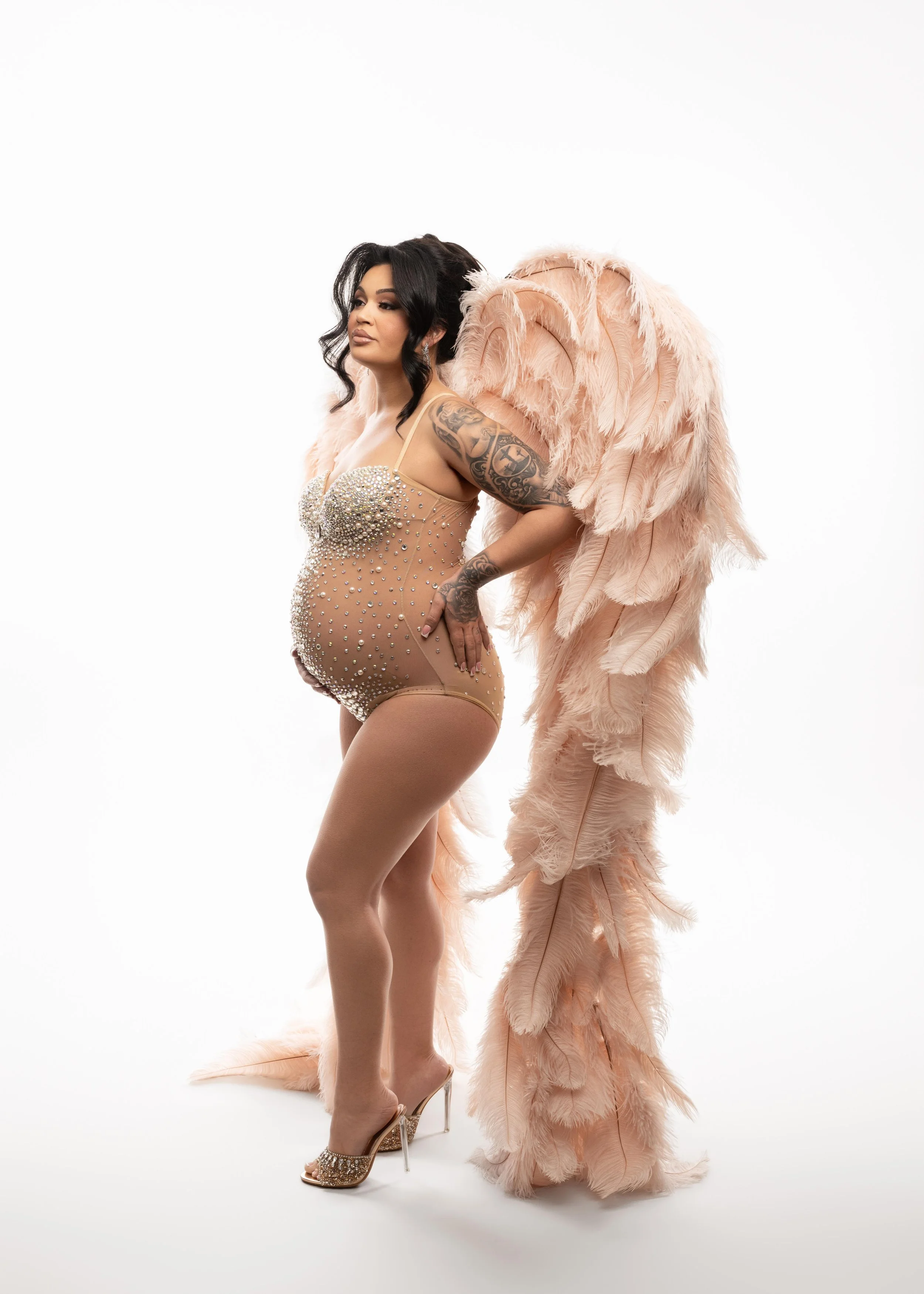 Fashion-inspired maternity portrait with dramatic feather wings and neutral styling, photographed in Frisco, Texas.