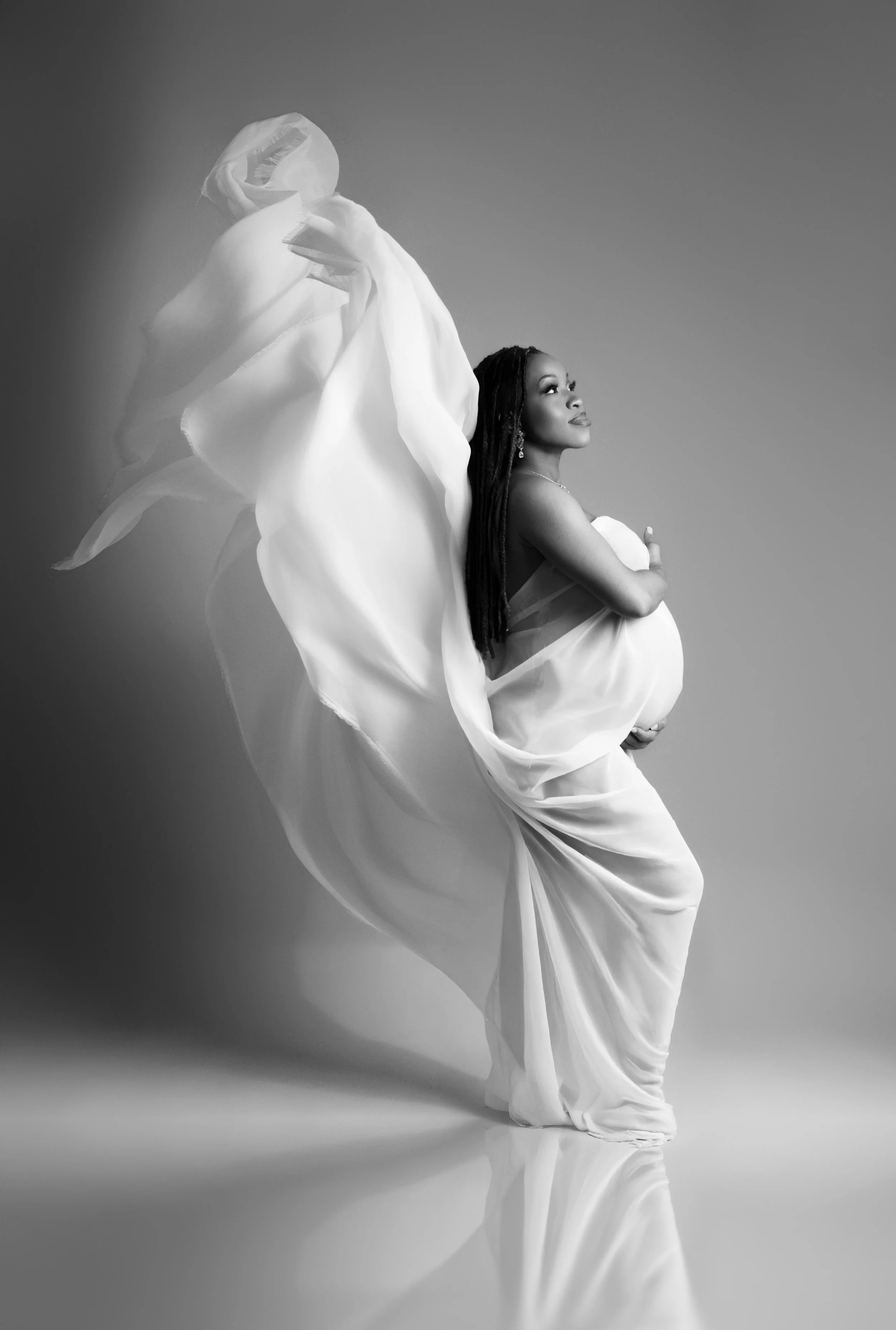 Fine art black and white maternity portrait with flowing fabric and dramatic movement, photographed in Dallas, Texas.