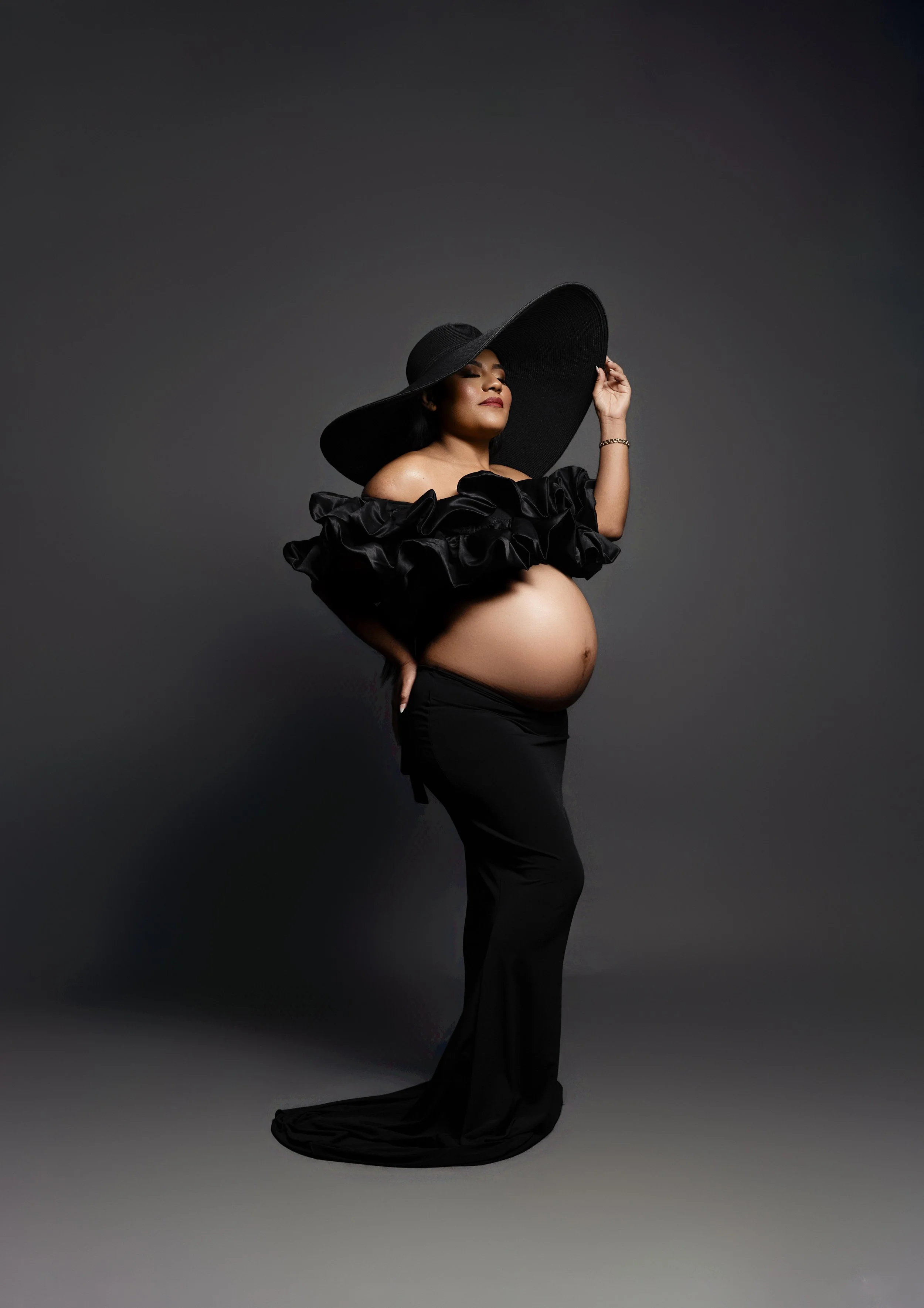 Fashion-inspired maternity portrait in a dramatic black gown and wide-brim hat, photographed in Dallas, Texas.