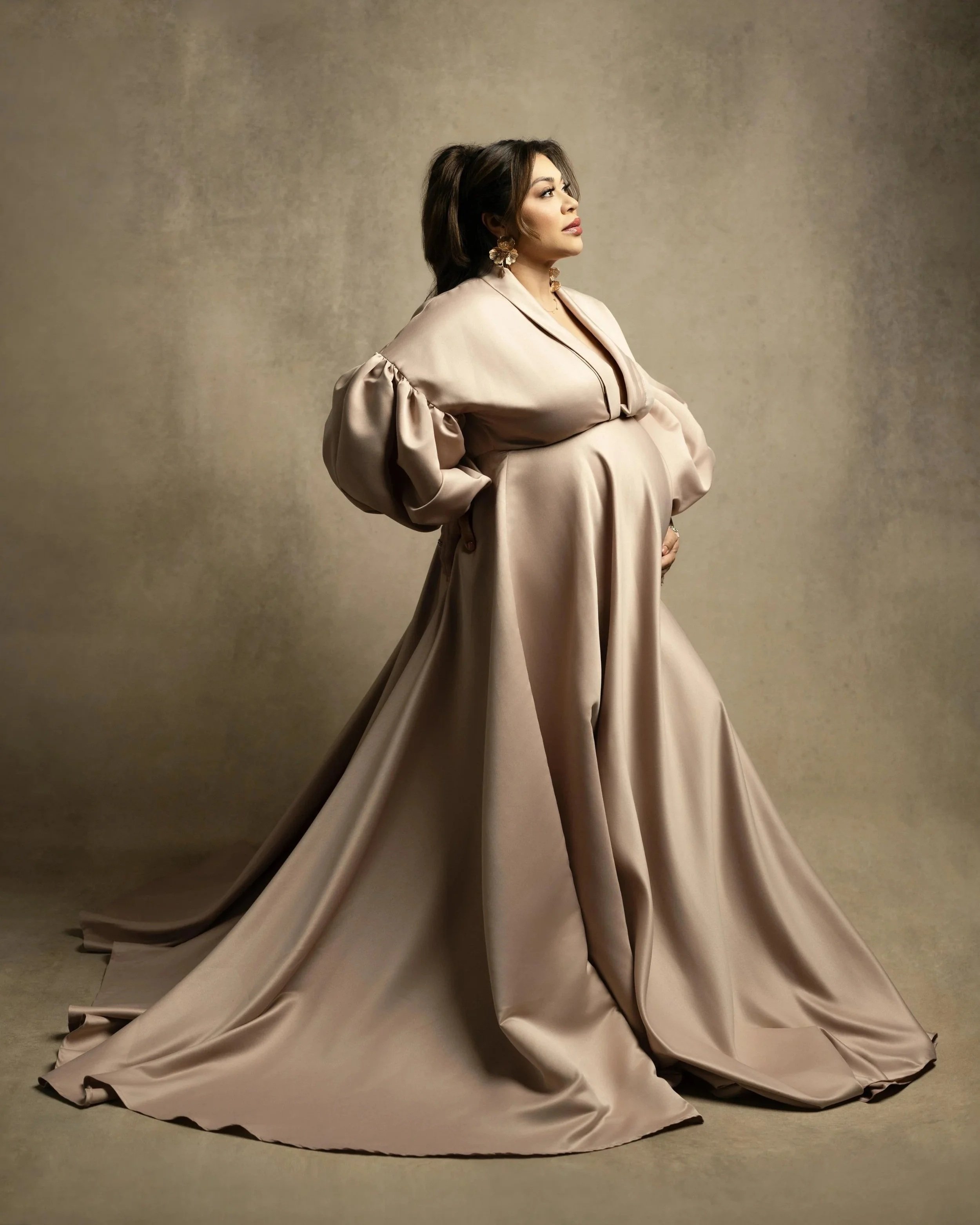 Pregnant woman in a flowing blush gown photographed in a Dallas maternity photography studio.